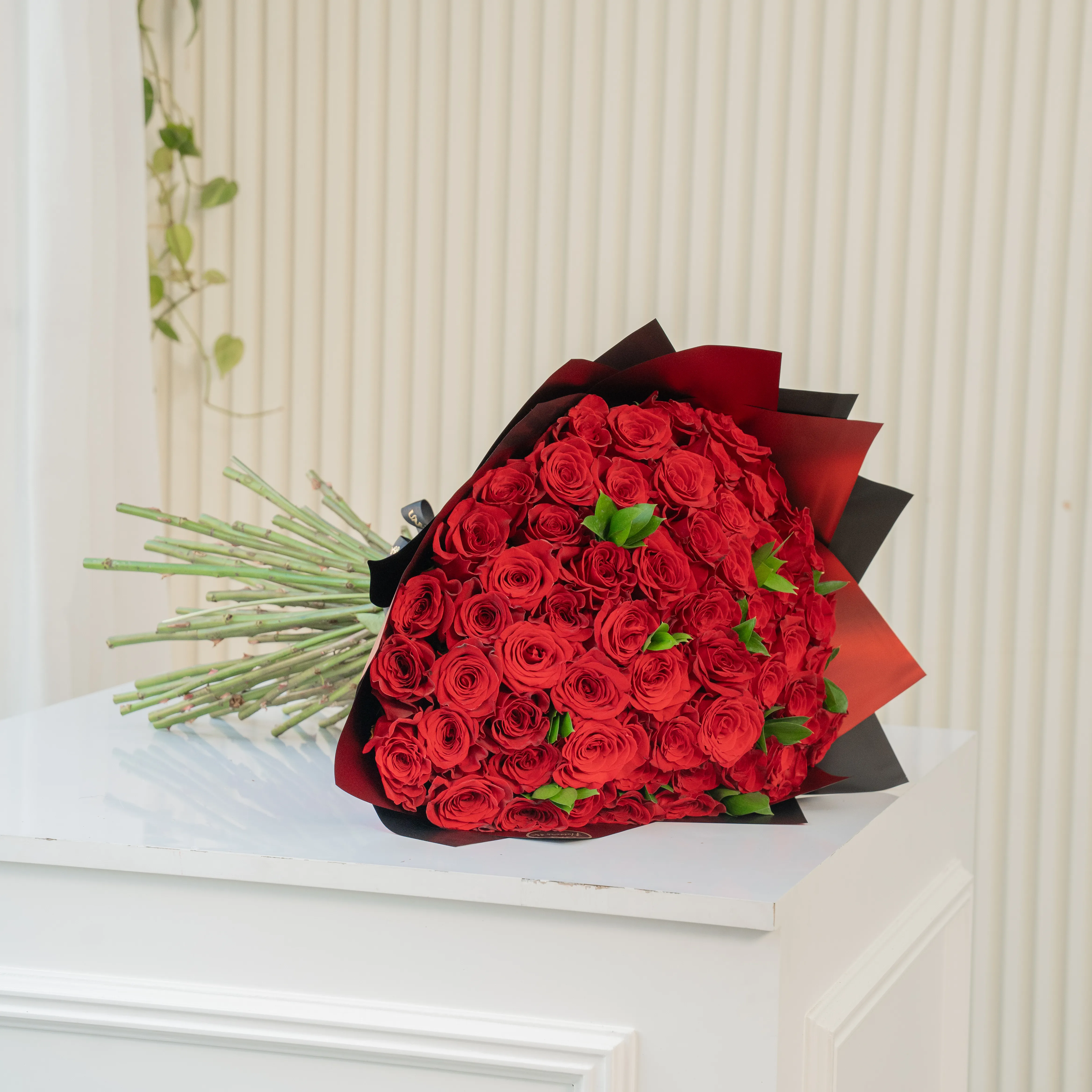Bouquet of 100 red roses in paper packing hand-tied with ribbons.