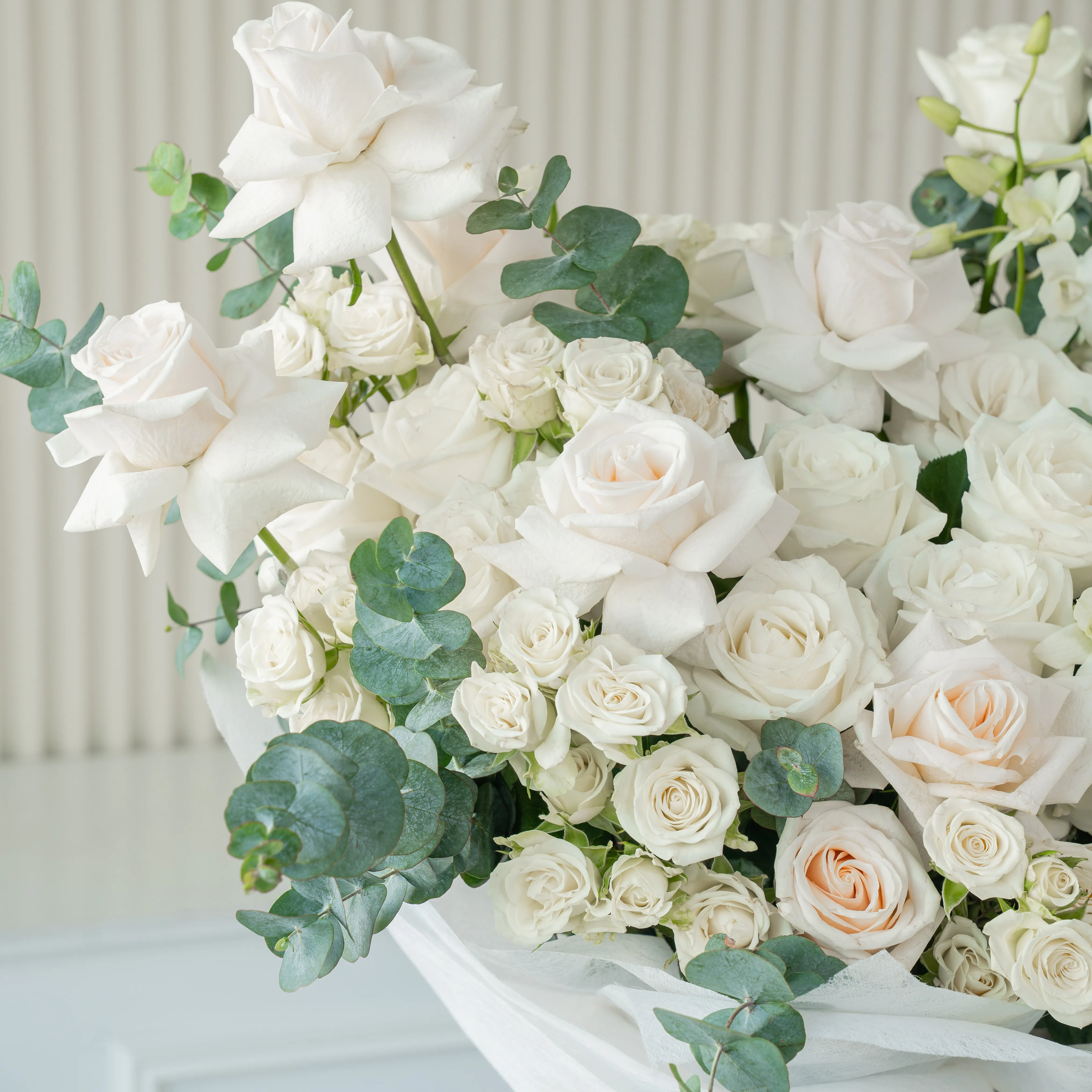 Bouquet of 20 white roses and 10 white spray roses with green fillers in white paper packing tied with white ribbon.