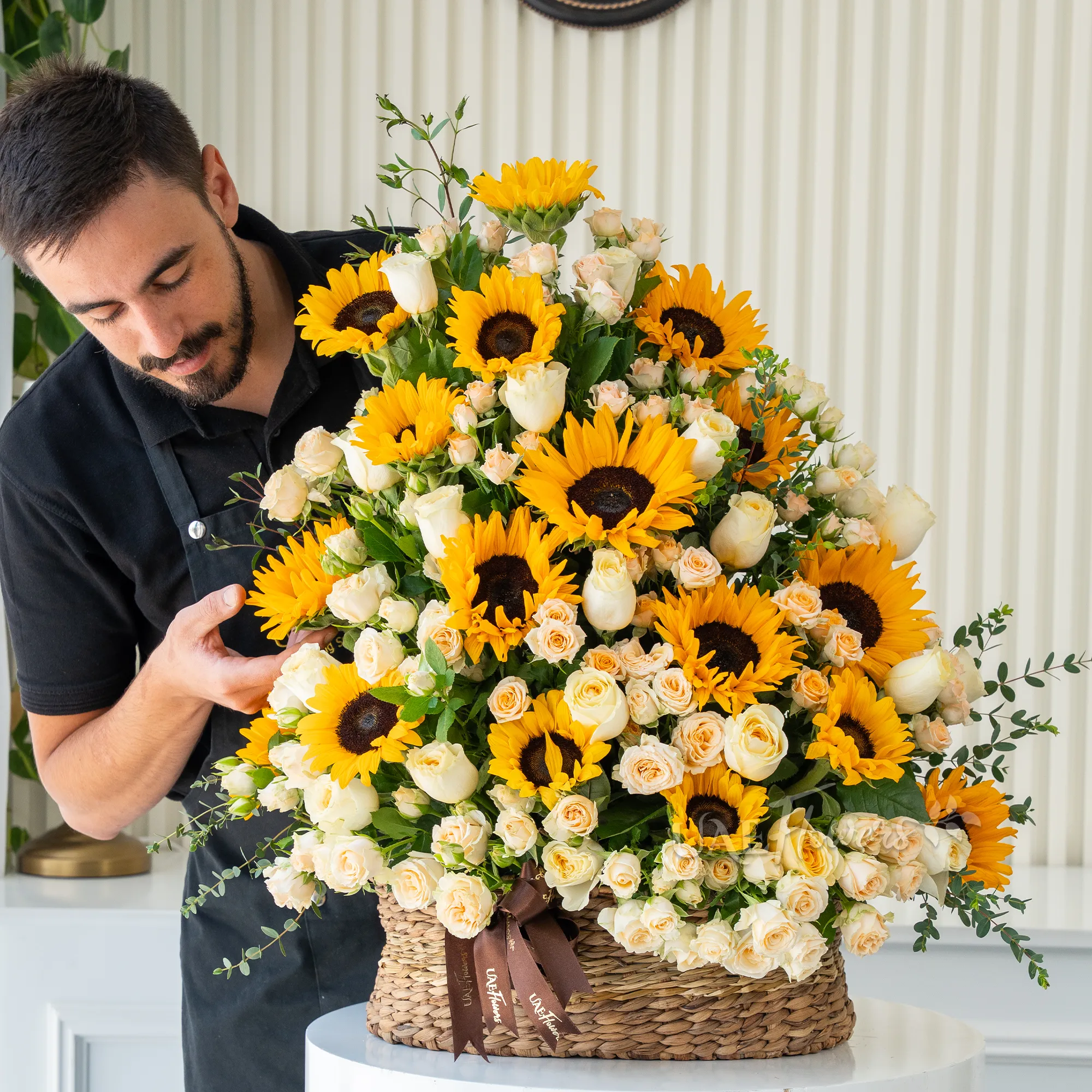 Basket arrangement of 15 sunflowers, 20 peach roses and 15 peach spray roses with fillers.