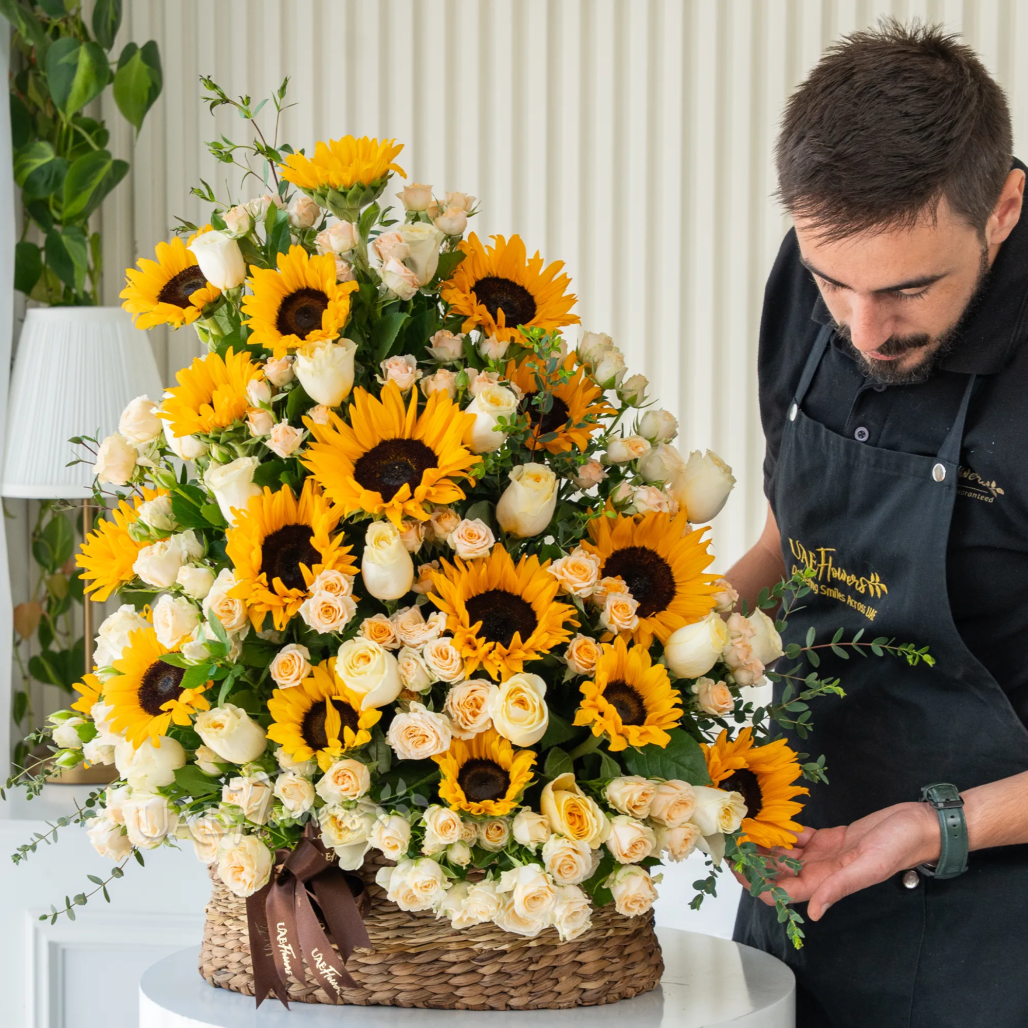 Basket arrangement of 15 sunflowers, 20 peach roses and 15 peach spray roses with fillers.