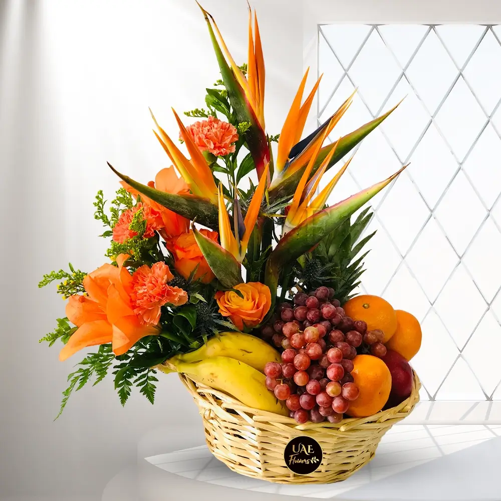 A basket of exotic golden flowers, a spiky bird of paradise, lilies, and plenty of the juiciest tropical fruits, including bananas, pineapple, apples, oranges, and grapes