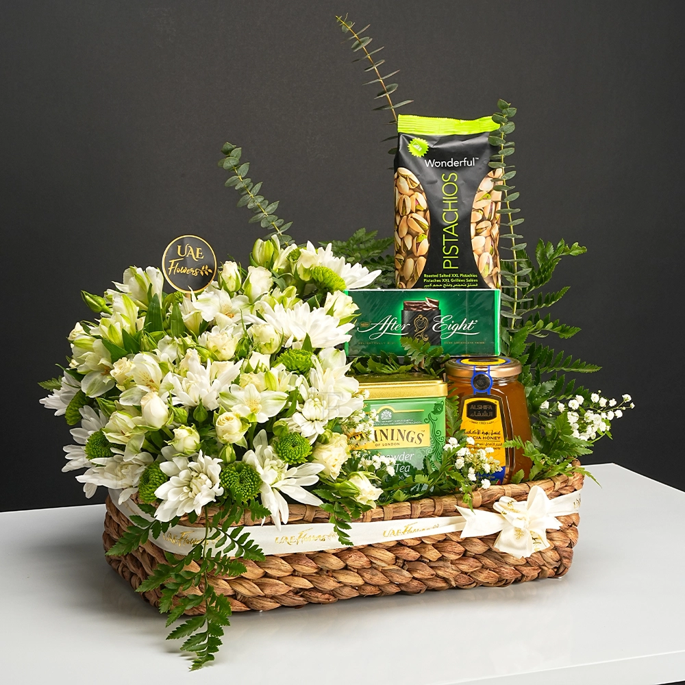 Elegant gift basket with white flowers, gourmet snacks, and tea wrapped in a white ribbon