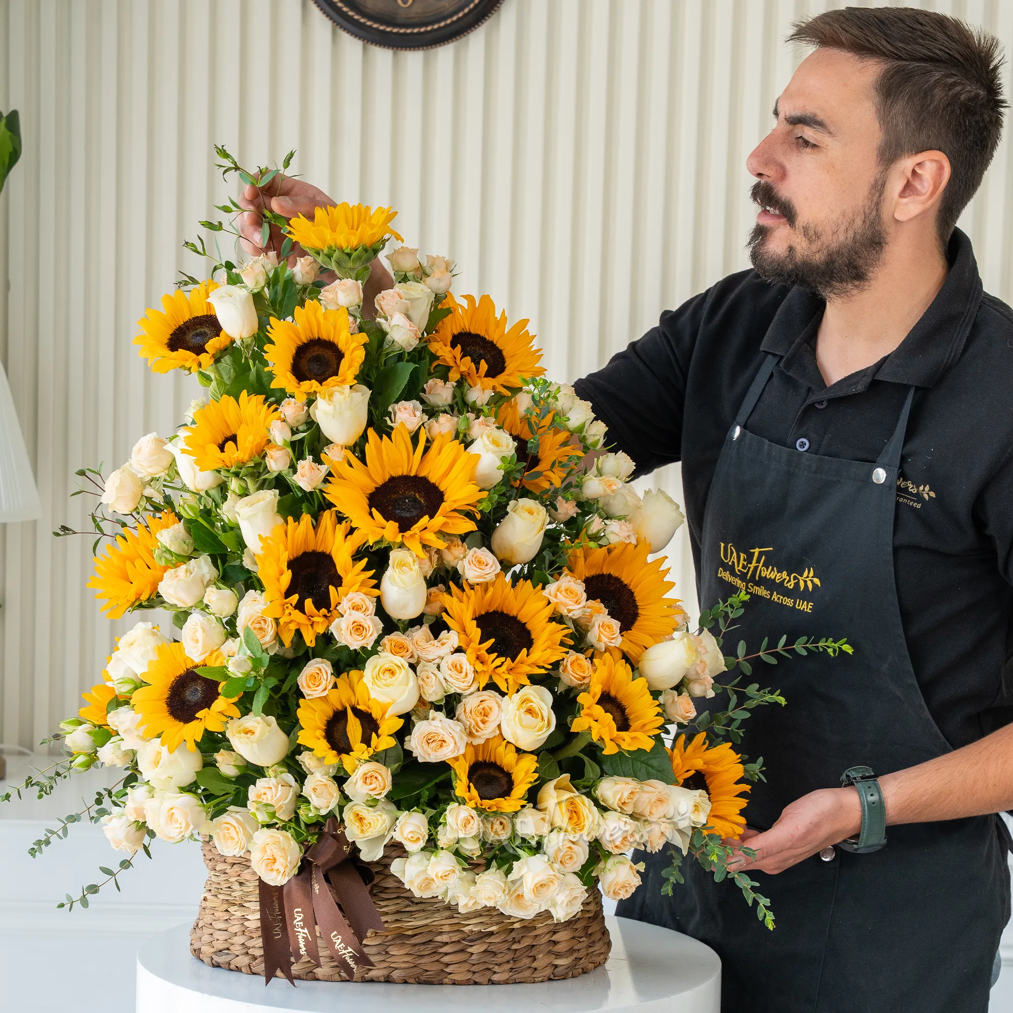 Basket arrangement of 15 sunflowers, 20 peach roses and 15 peach spray roses with fillers.