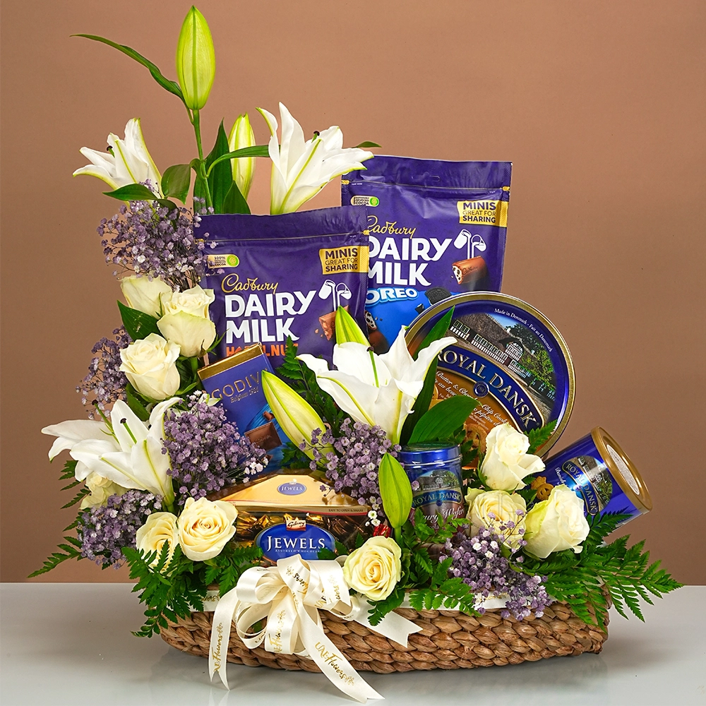 gift hamper with chocolates, cookies, white lilies, roses, and baby’s breath in a basket