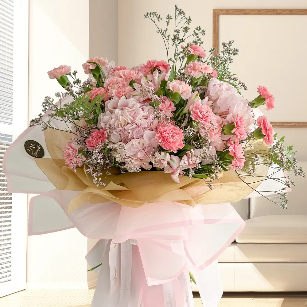 A bouquet of 2 pink hydrangeas, 20 pink carnations and 5 pink alstroemeria with fillers in pink and brown wrapping paper tied with pink ribbon