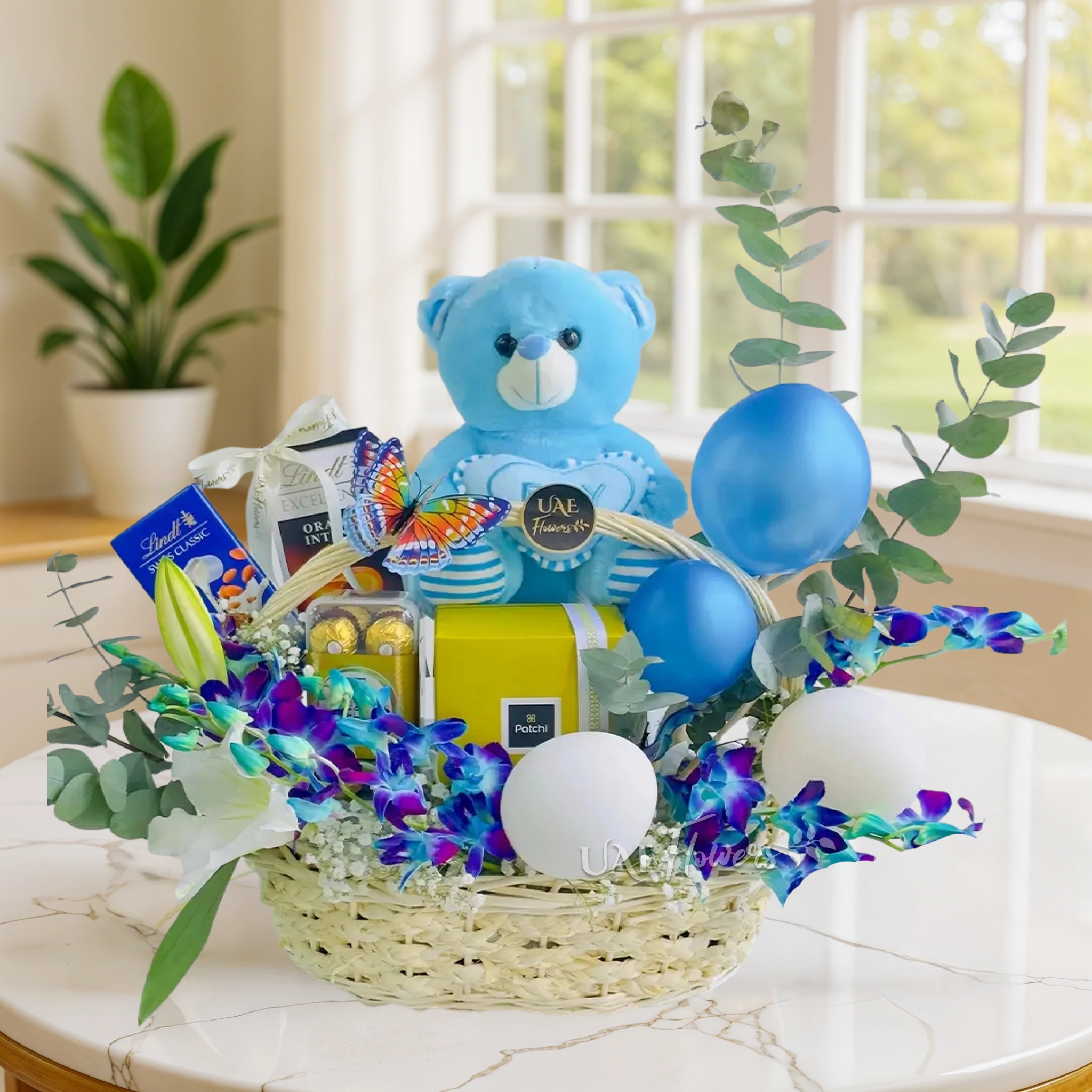 Baby Boy Blue Gift Basket includes a white lily, blue orchids, and a mix of chocolates
