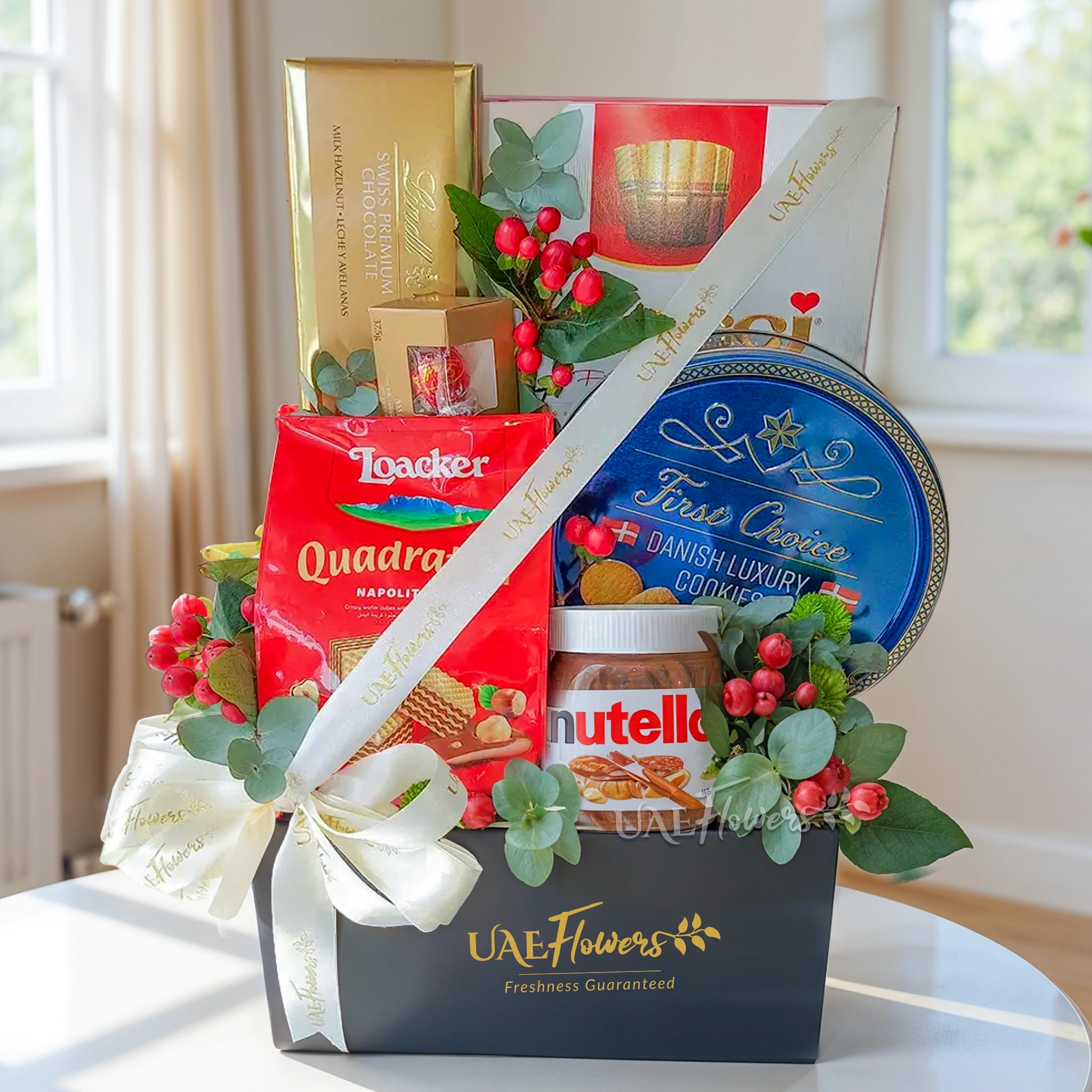 A gift hamper containing chocolates & cookies, along with 2 gold hypericum greens & fillers, all presented in a black box