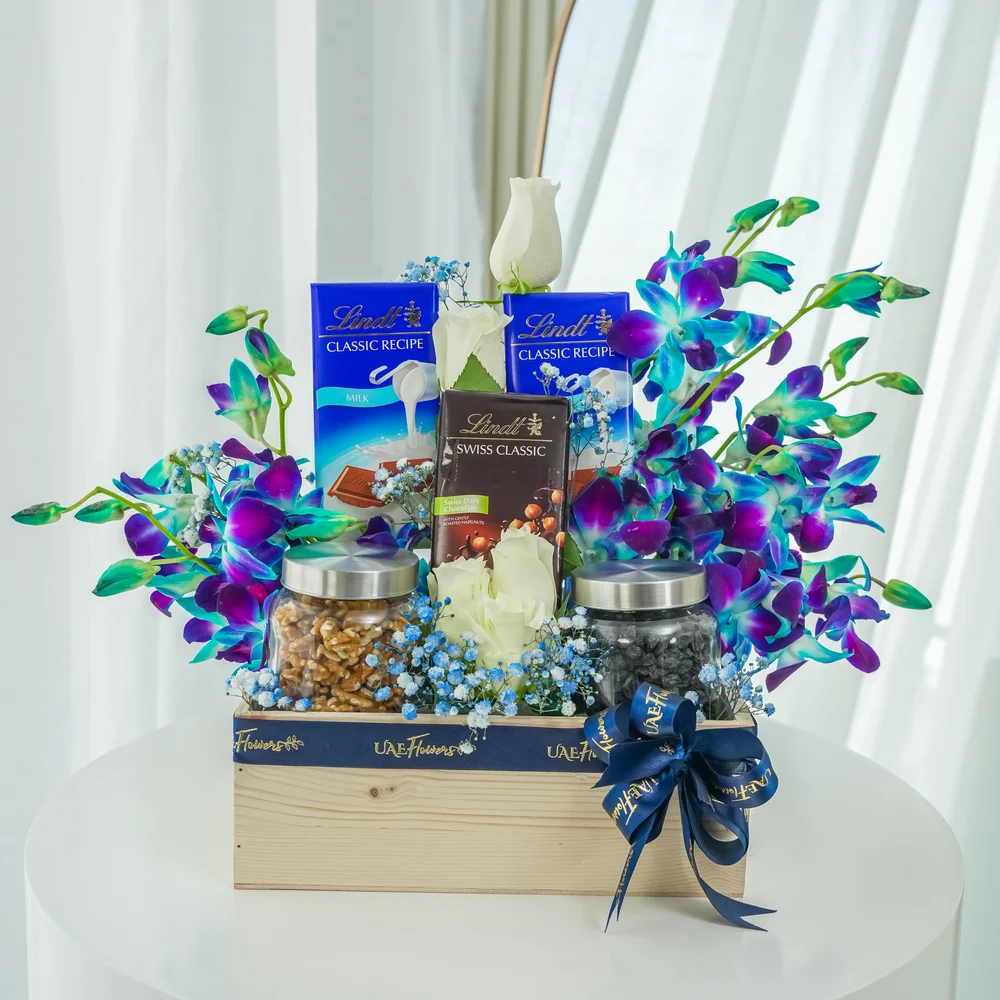 An arrangement of 5 white roses and 5 blue orchids, 250 Gms of Walnuts and 250 Gms of black raisins with 2 pcs of Lindt Swiss Classic Milk Chocolate, Lindt Swiss Classic Dark Chocolate with baby's breath fillers in a wooden box.