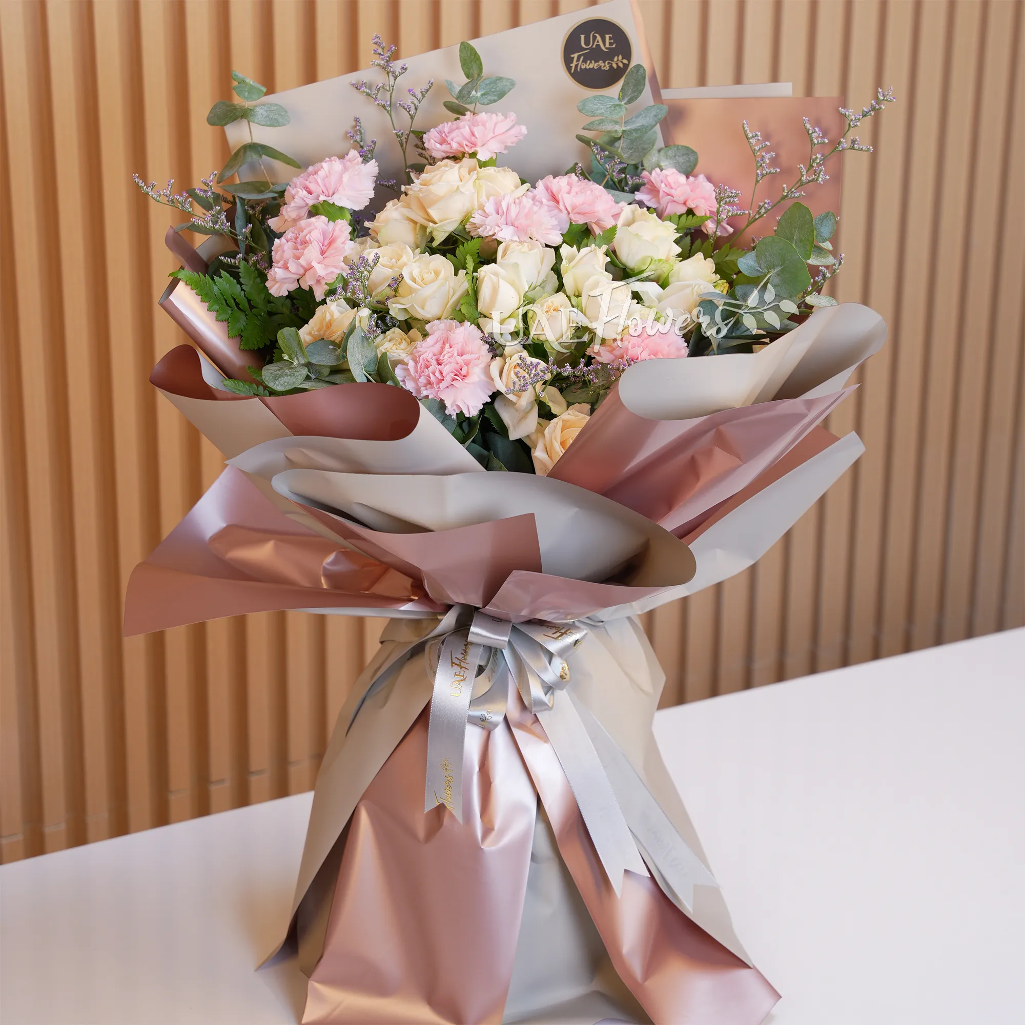 Bouquet of 8 pink carnations, 5 peach spray roses with green fillers in paper packing with ribbons, 1 kg black forest cake and a small brown teddy bear.
