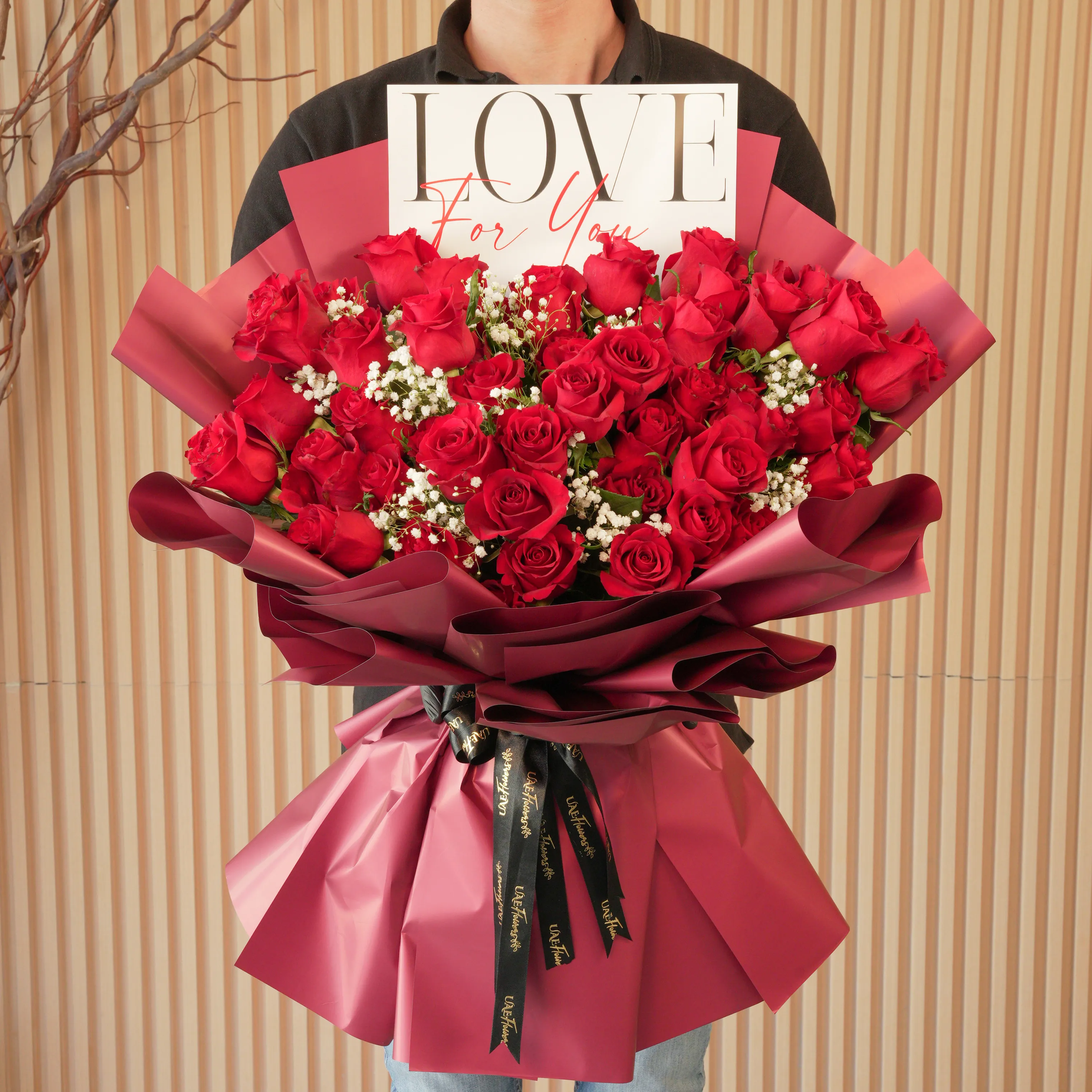 Bouquet of 50 red roses with baby’s breath fillers in red paper wrapping tied with black ribbons