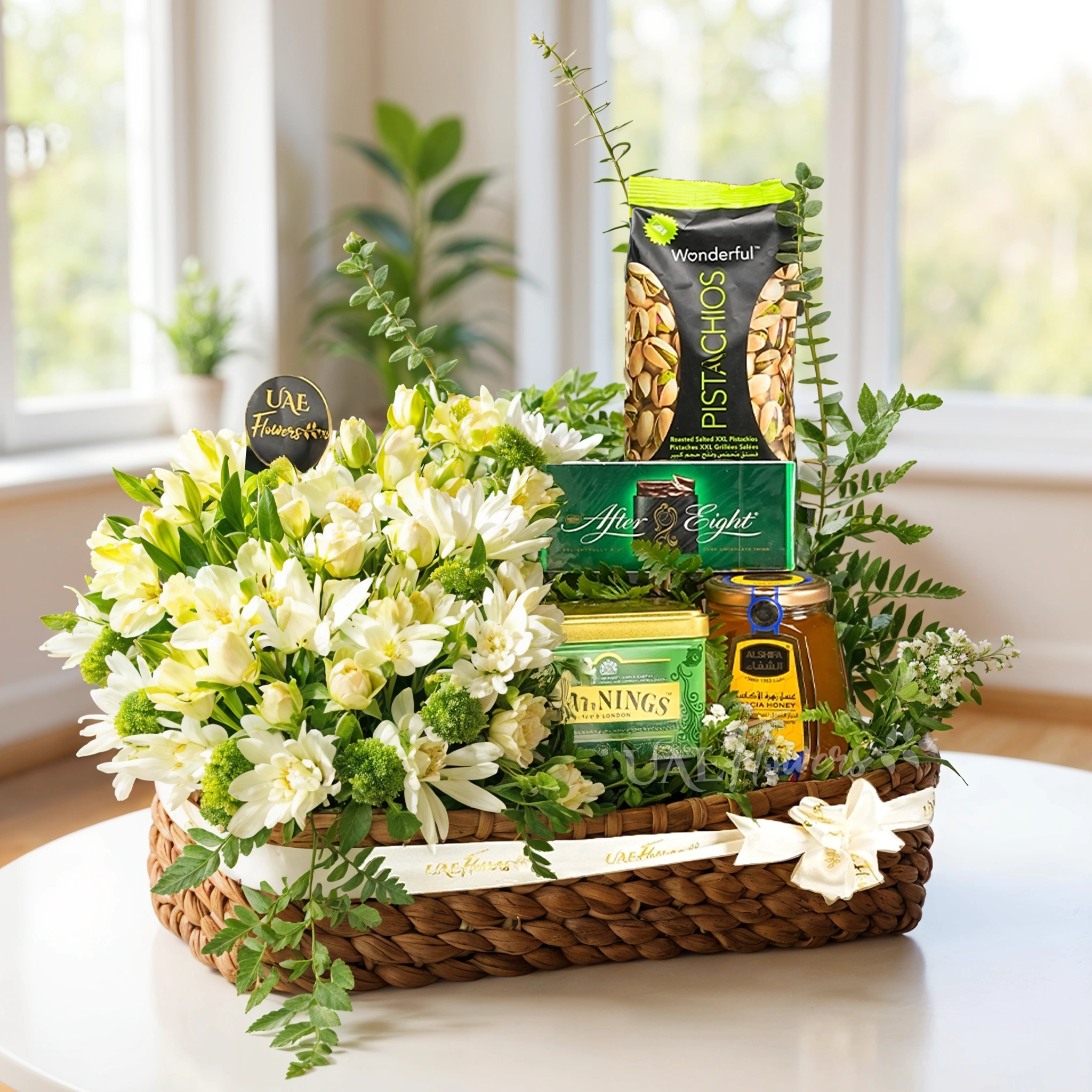 Elegant gift basket with white flowers, gourmet snacks, and tea wrapped in a white ribbon