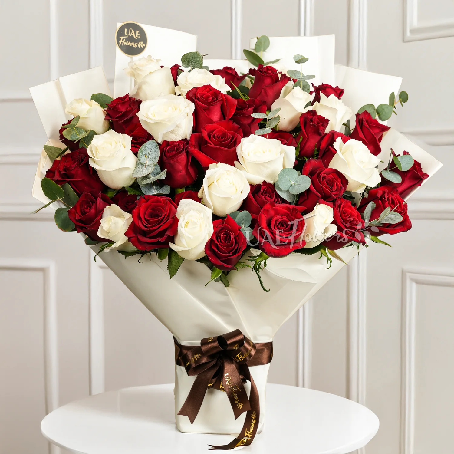 bouquet of 25 red and 15 white roses with green fillers in paper packing tied with ribbons