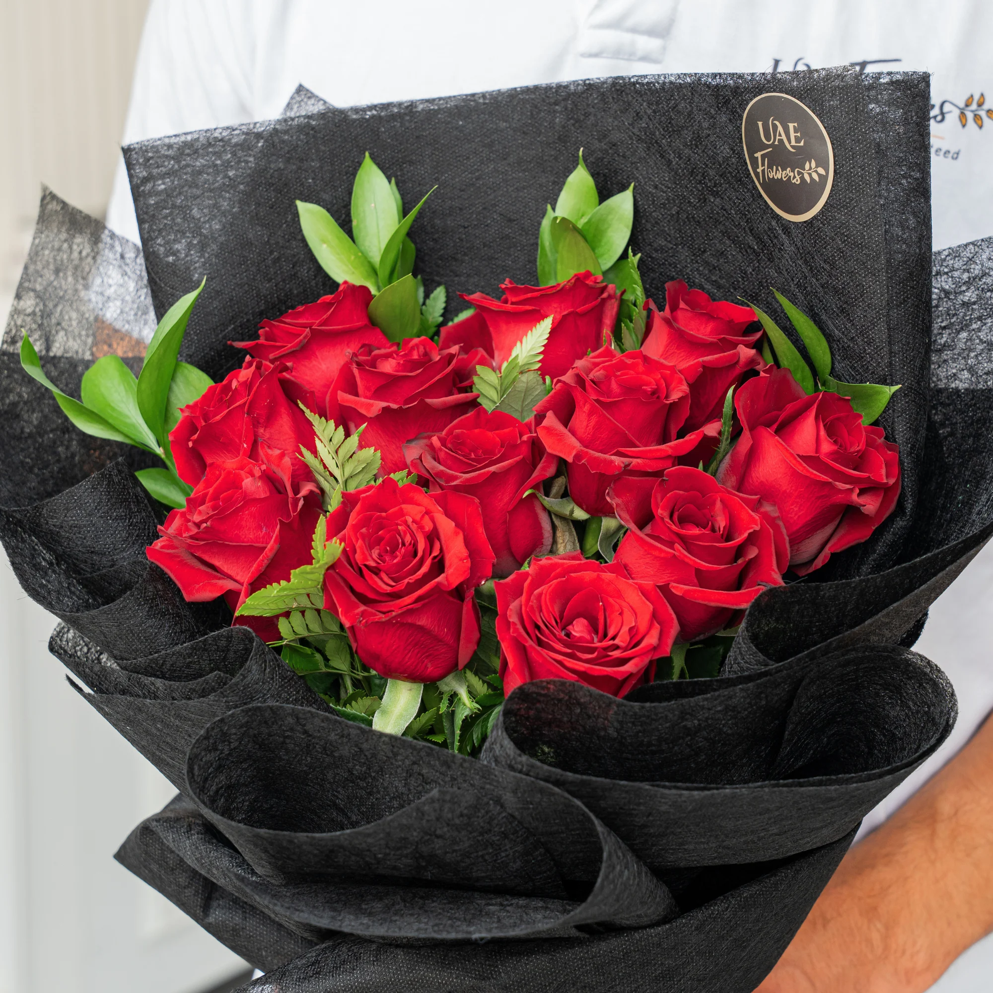 Bouquet of 12 red roses with green fillers in black wrapping paper.