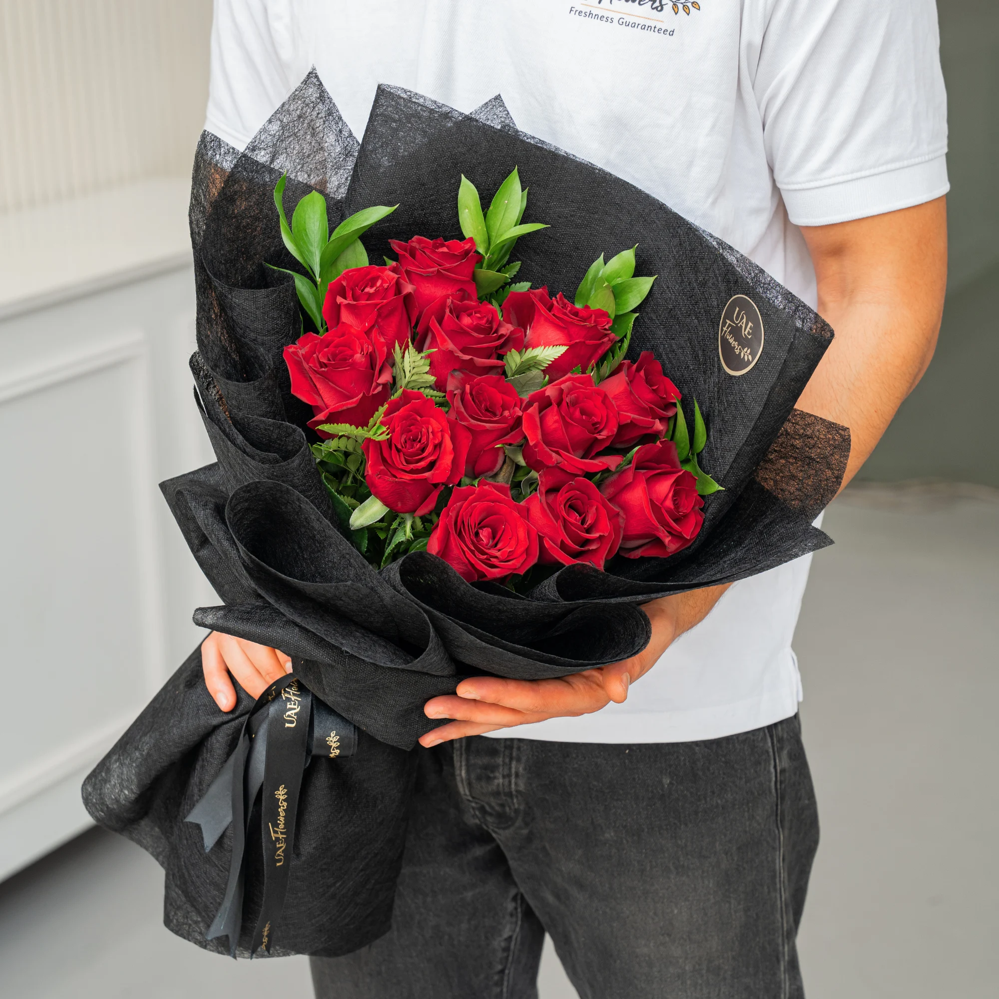 Bouquet of 12 red roses with green fillers in black wrapping paper.