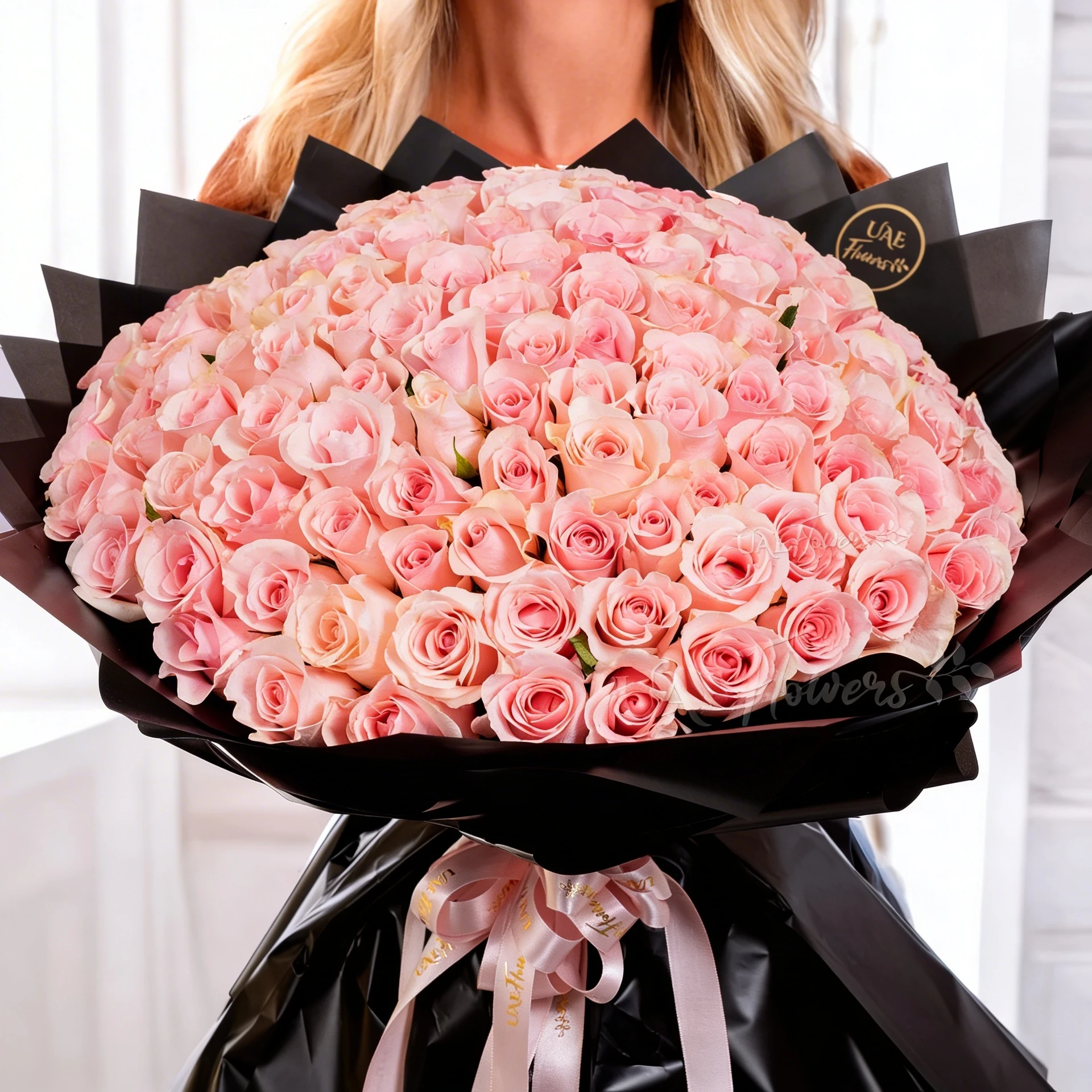 A 100-pink rose bouquet wrapped in black paper and tied with a white ribbon