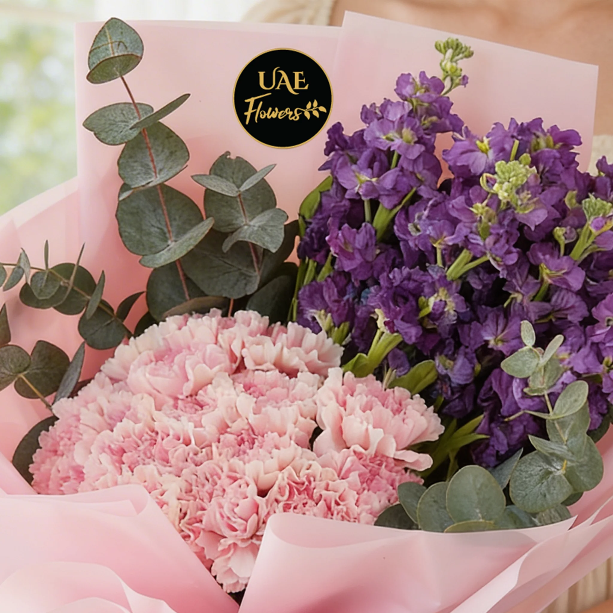 Bouquet of 10 purple matthiola and 15 pink carnations with green fillers in pink wrapping.
