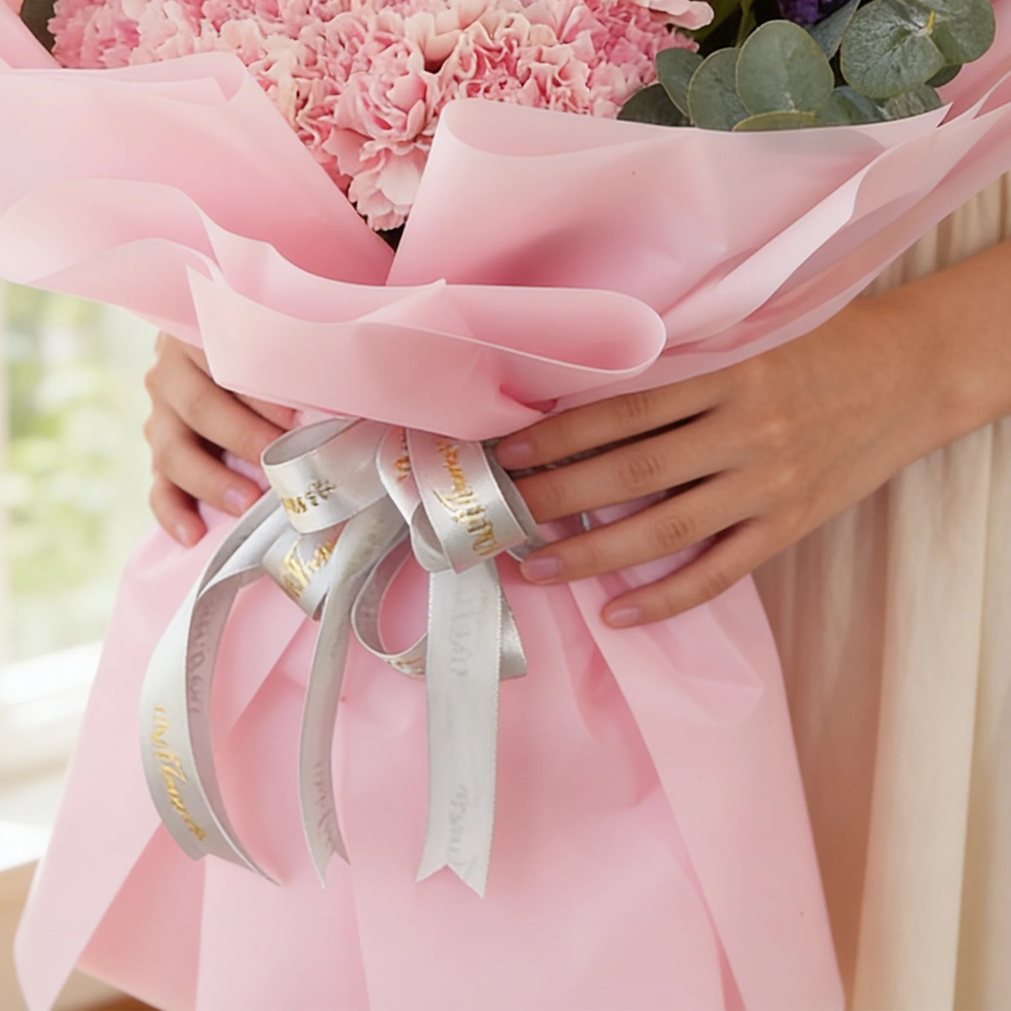 Bouquet of 10 purple matthiola and 15 pink carnations with green fillers in pink wrapping.