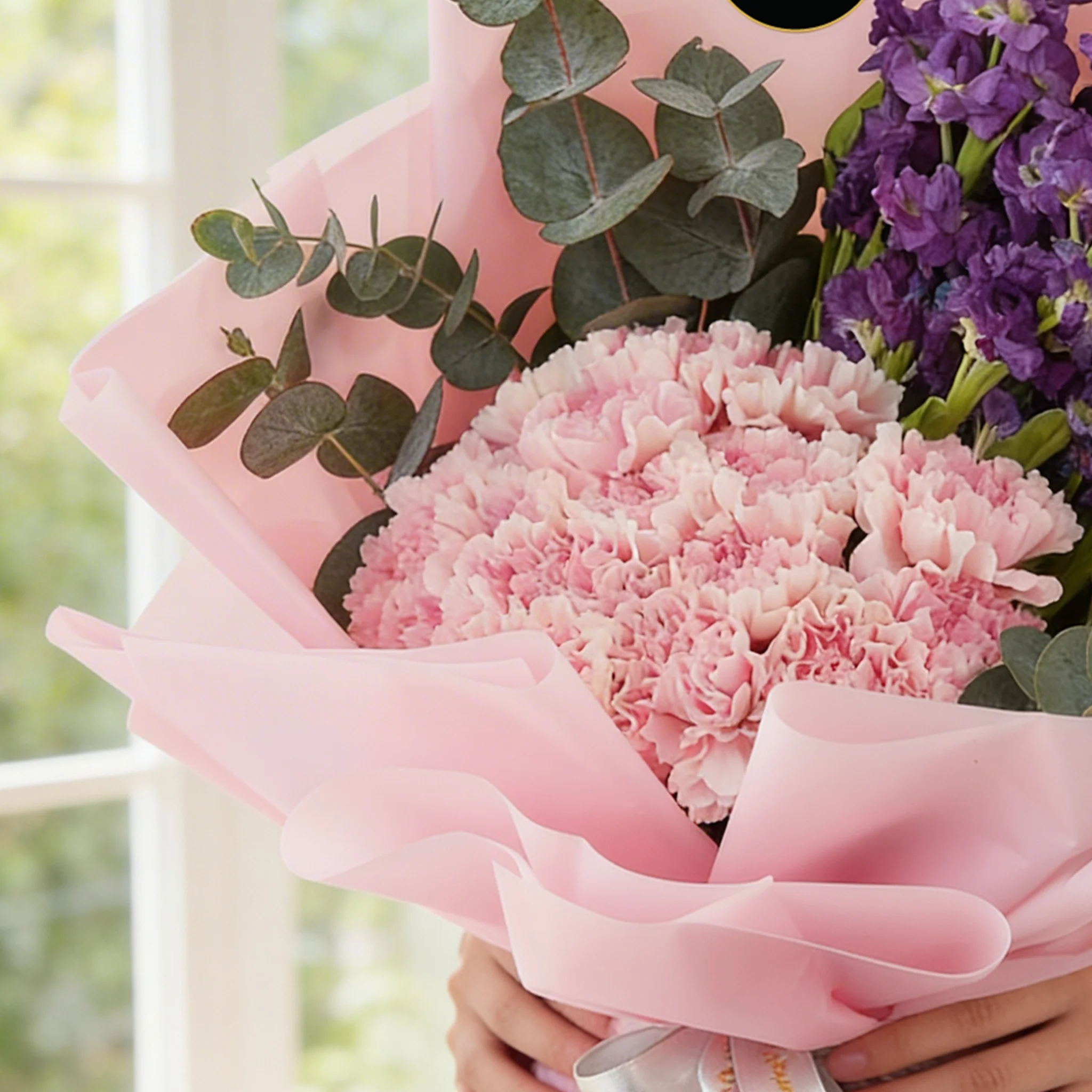Bouquet of 10 purple matthiola and 15 pink carnations with green fillers in pink wrapping.