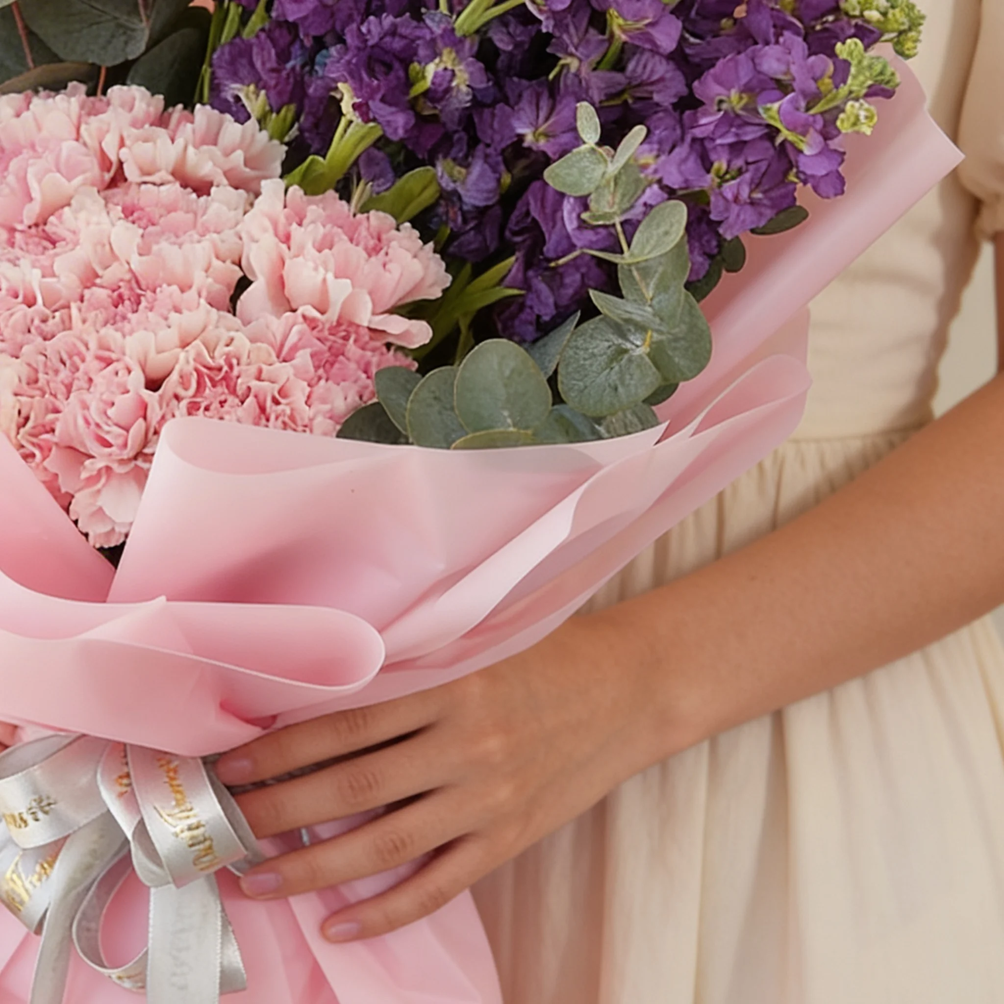 Bouquet of 10 purple matthiola and 15 pink carnations with green fillers in pink wrapping.