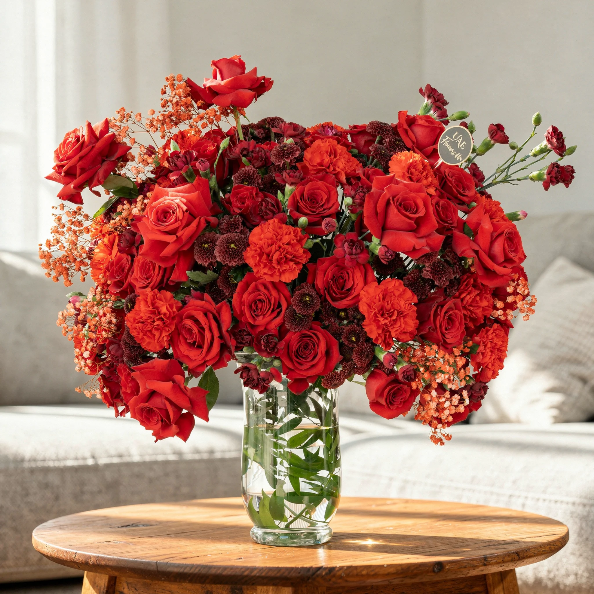 One-side arrangement of 20 red roses, 7 red chrysanthemums, 8 red carnations and 4 red spray carnations with green fillers in a glass vase.