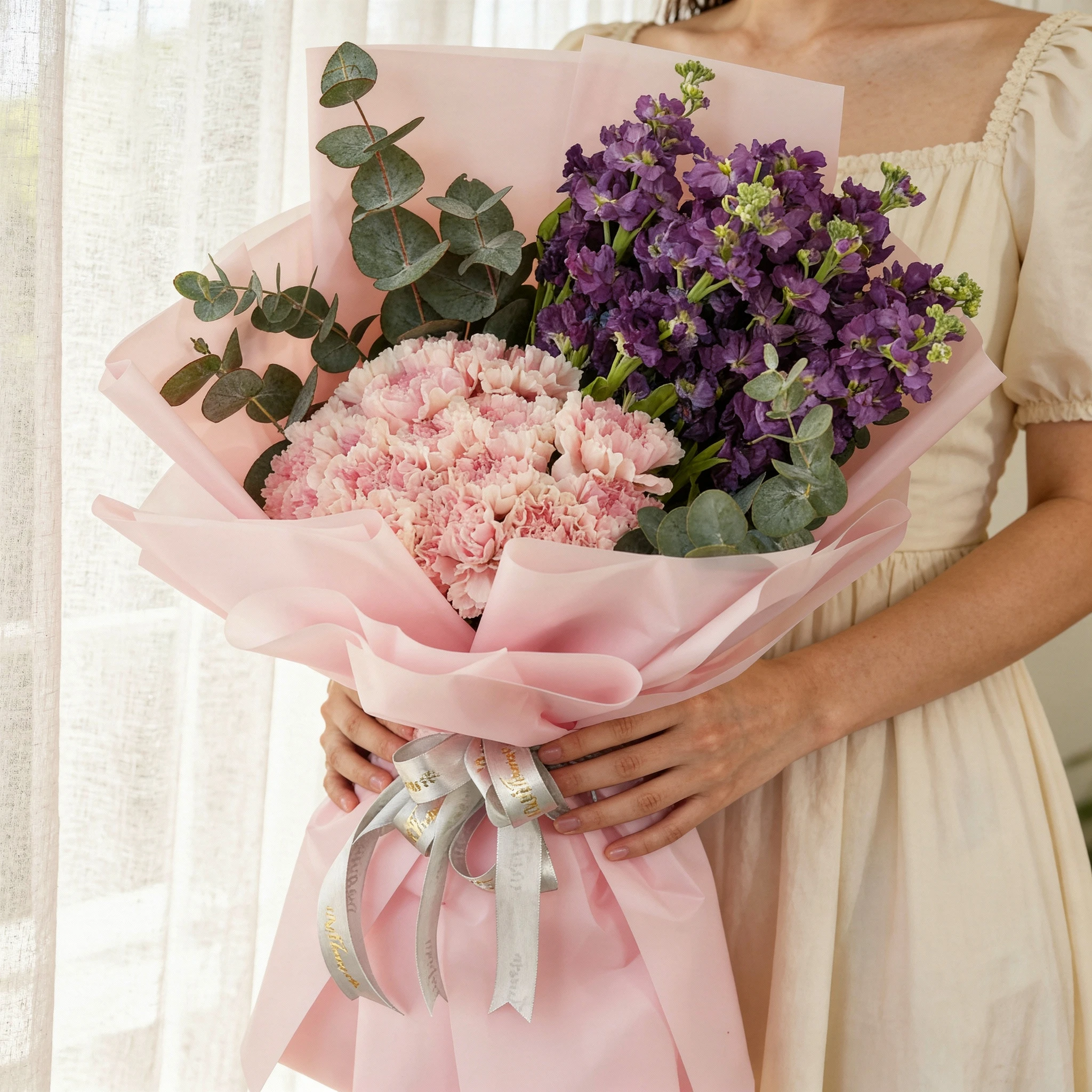 Bouquet of 10 purple matthiola and 15 pink carnations with green fillers in pink wrapping.
