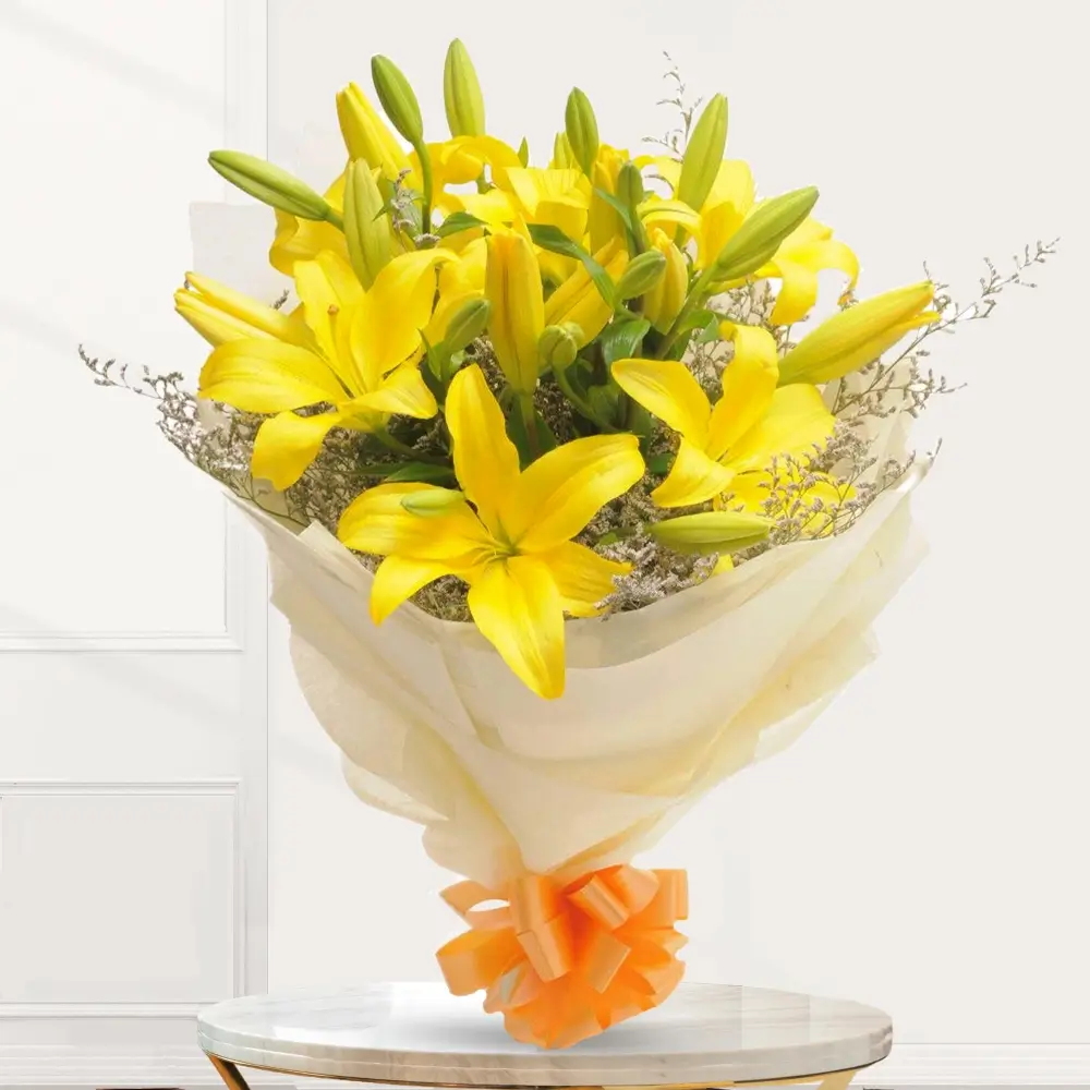 Bouquet of 7 yellow lilies with greens in white wrapping paper with a orange ribbon