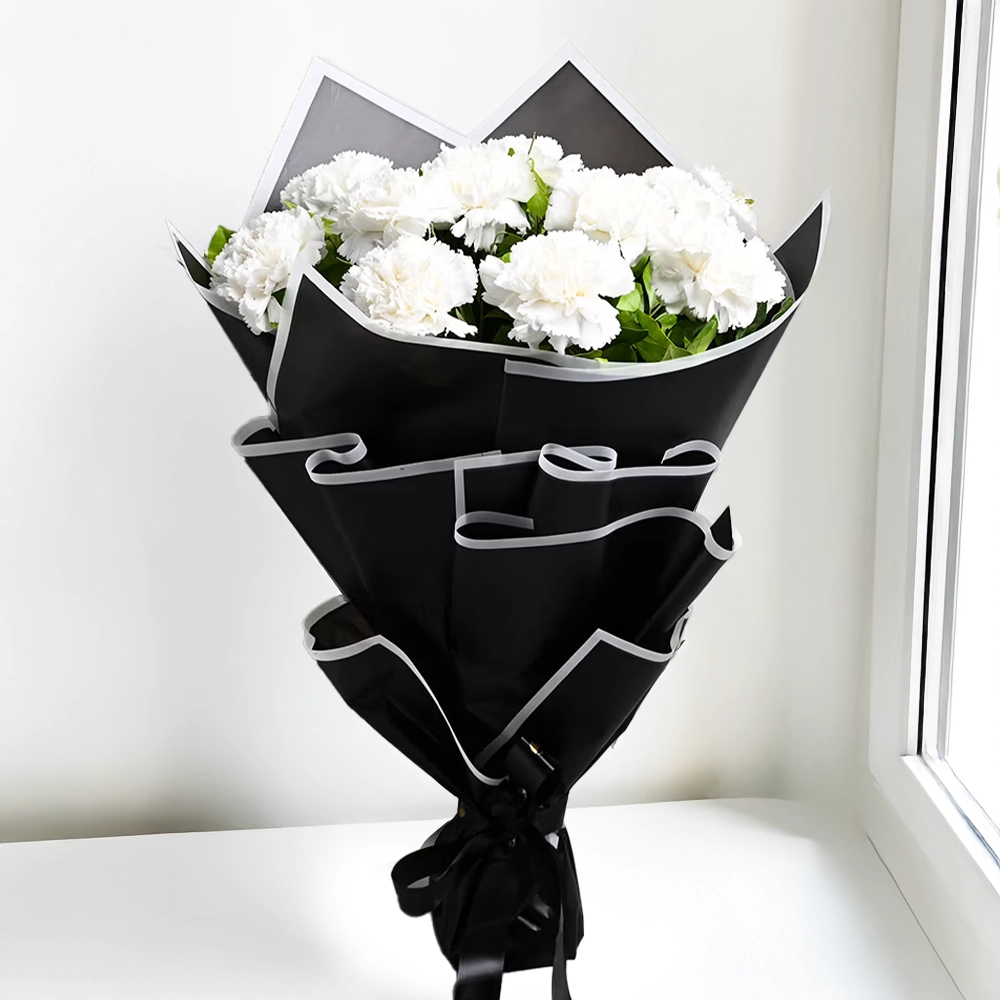 Pure Elegance - Bouquet of 15 fresh white carnations with fillers, wrapped in soft white paper, placed on a light surface by a window.