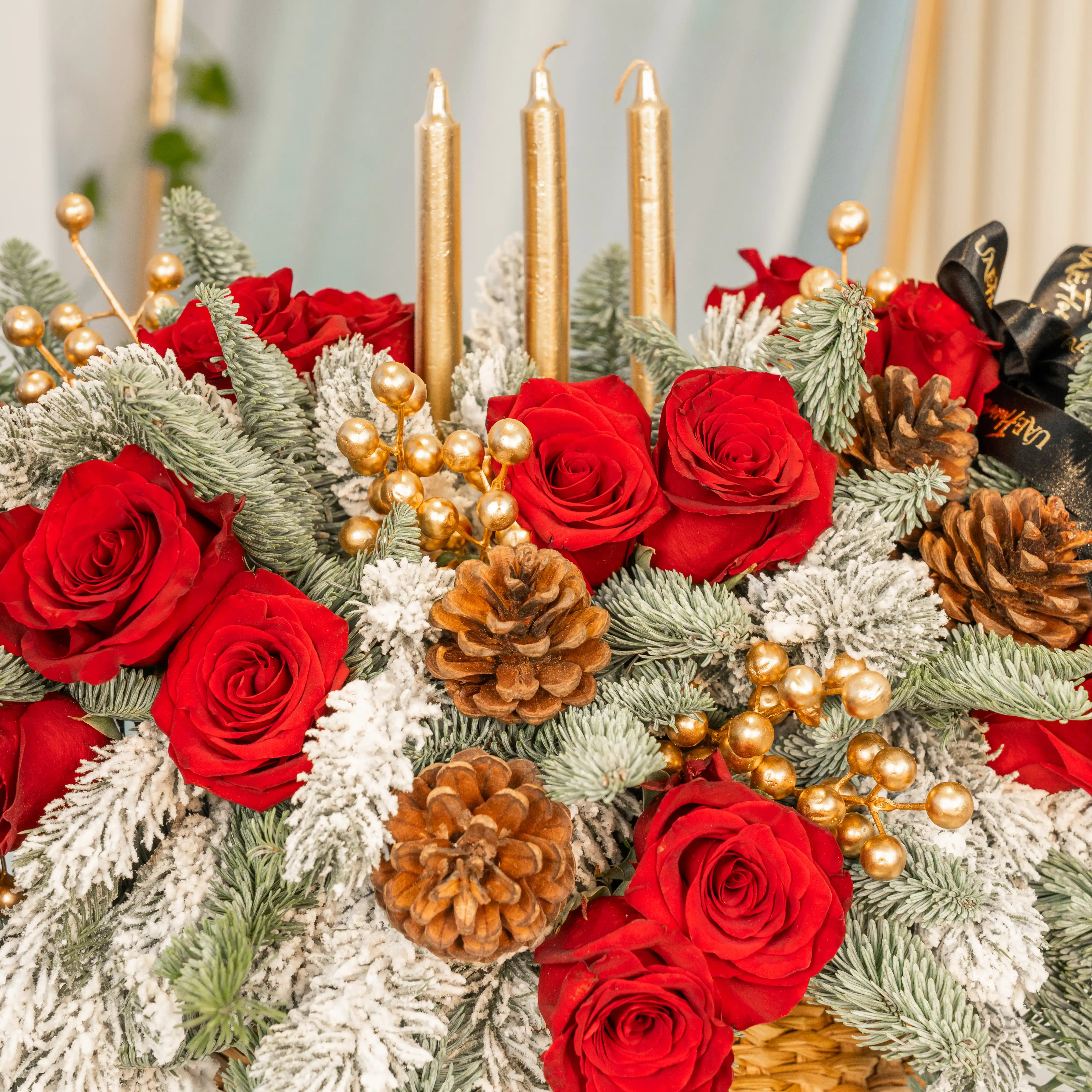 Christmas centerpiece with red roses, snowy pine, gold candles, pinecones in a woven basket
