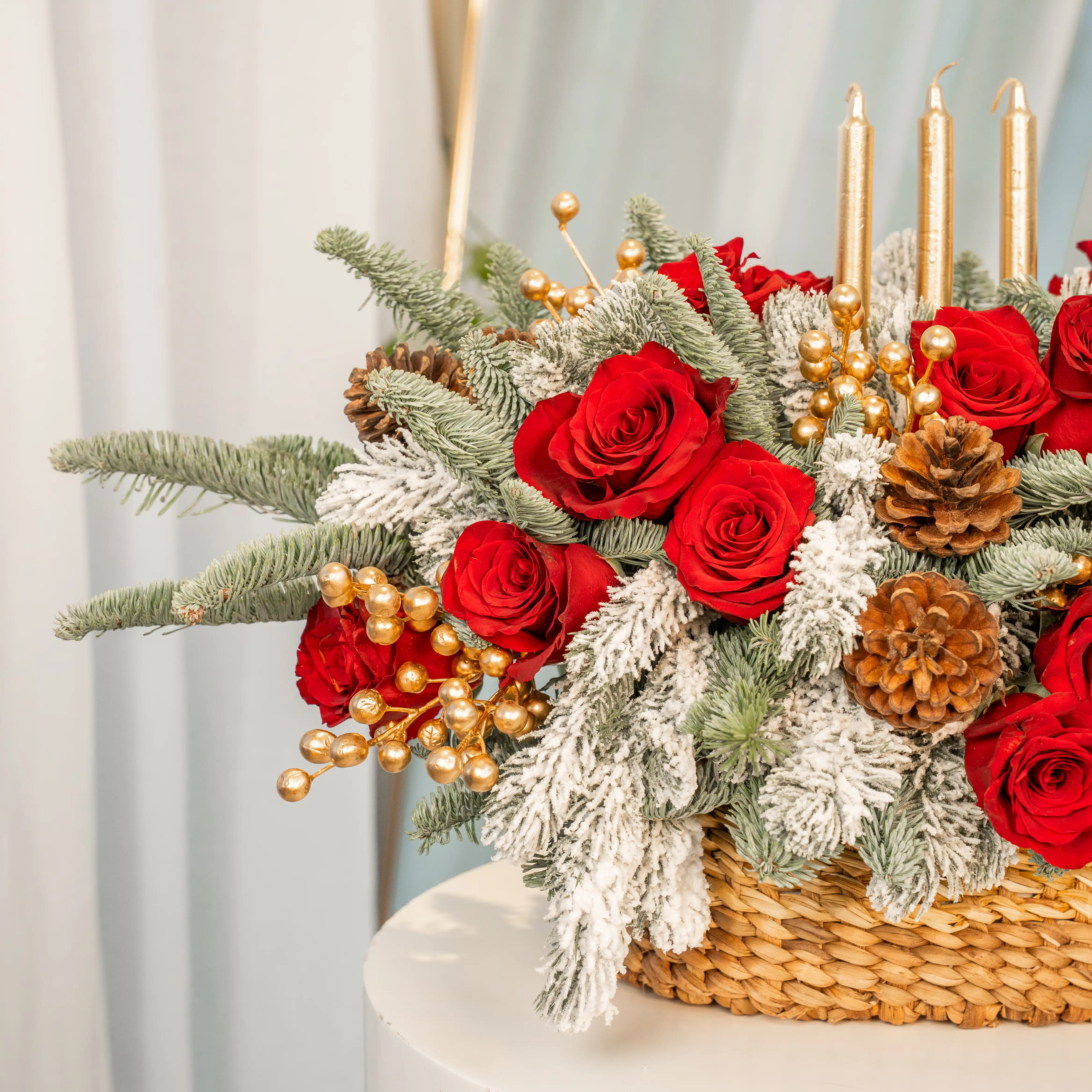 Christmas centerpiece with red roses, snowy pine, gold candles, pinecones in a woven basket