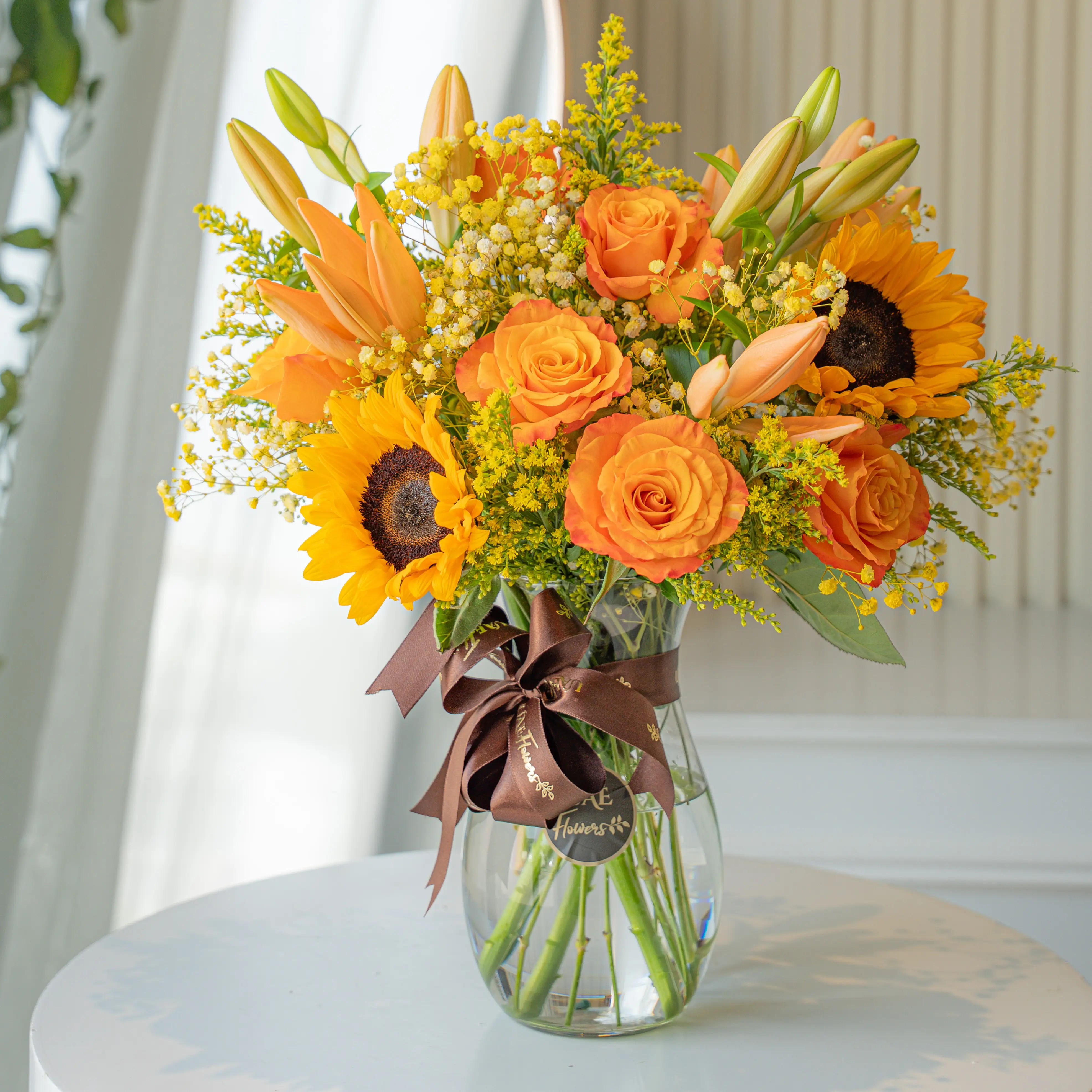 Sunflowers, orange roses, and lilies in a glass vase for Diwali by UAE Flowers Dubai
