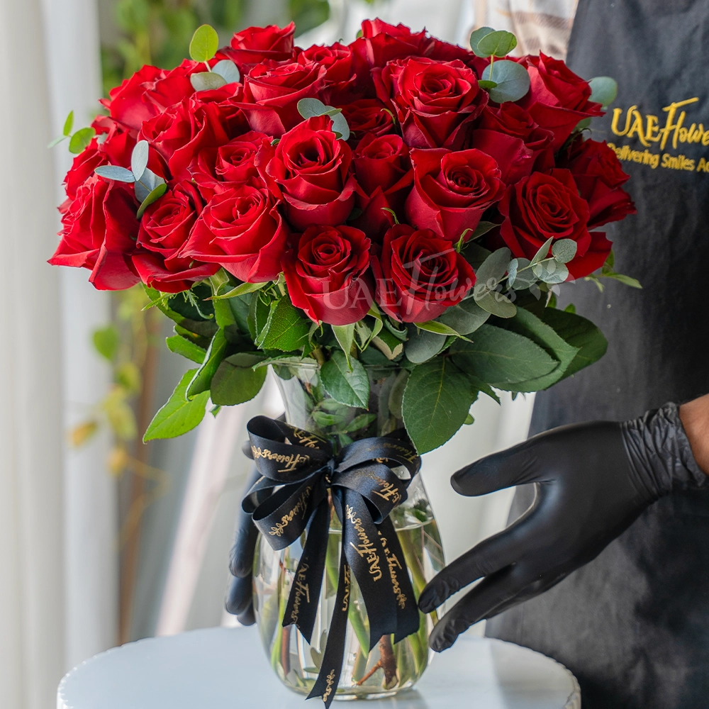30 red roses arranged in a clear vase with eucalyptus leaves
