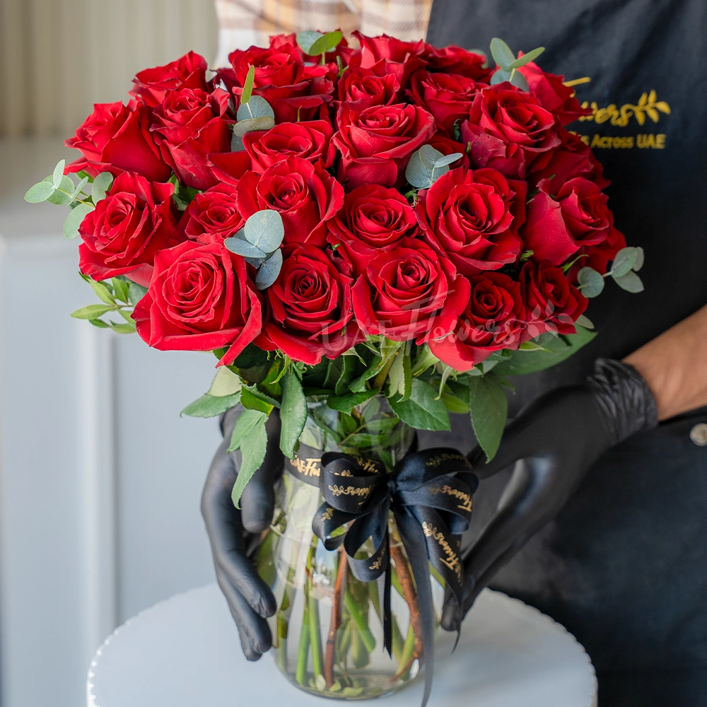 30 red roses arranged in a clear vase with eucalyptus leaves