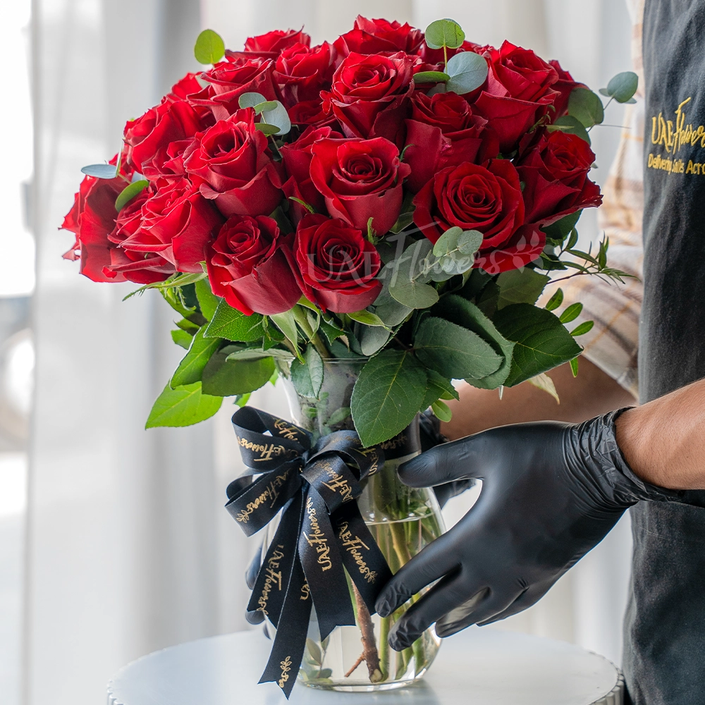 30 red roses arranged in a clear vase with eucalyptus leaves