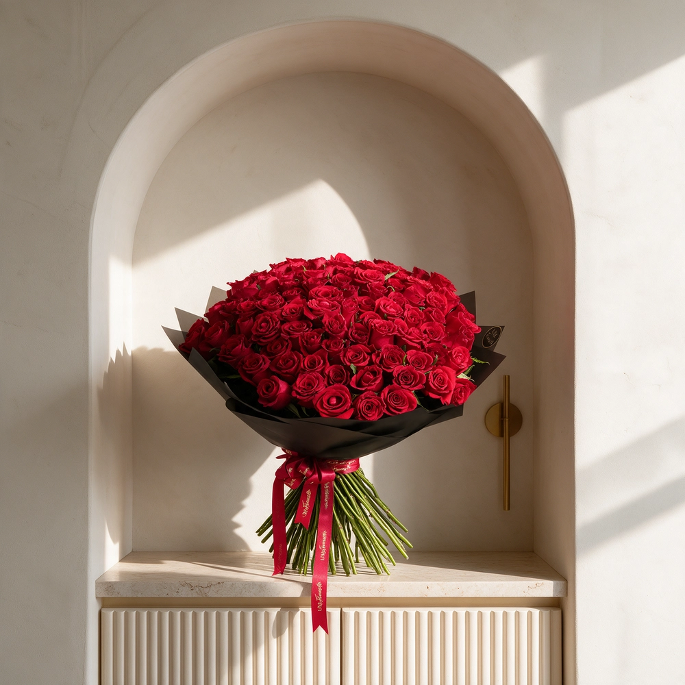 100 premium red roses hand-tied with green fillers and wrapped in black paper with satin ribbon