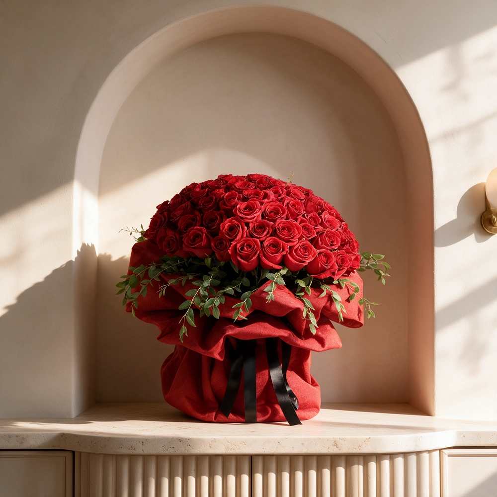 A large bouquet featuring 40 vibrant red roses paired with delicate gypsophila (baby's breath) elegantly wrapped in cream-colored paper and tied with a bold red ribbon, sitting on a table in a modern