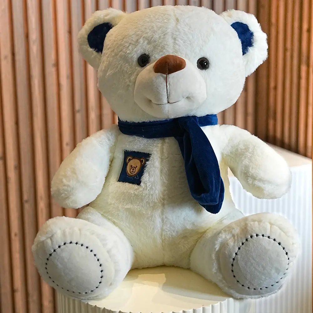 A medium size white teddy bear with a blue scarf