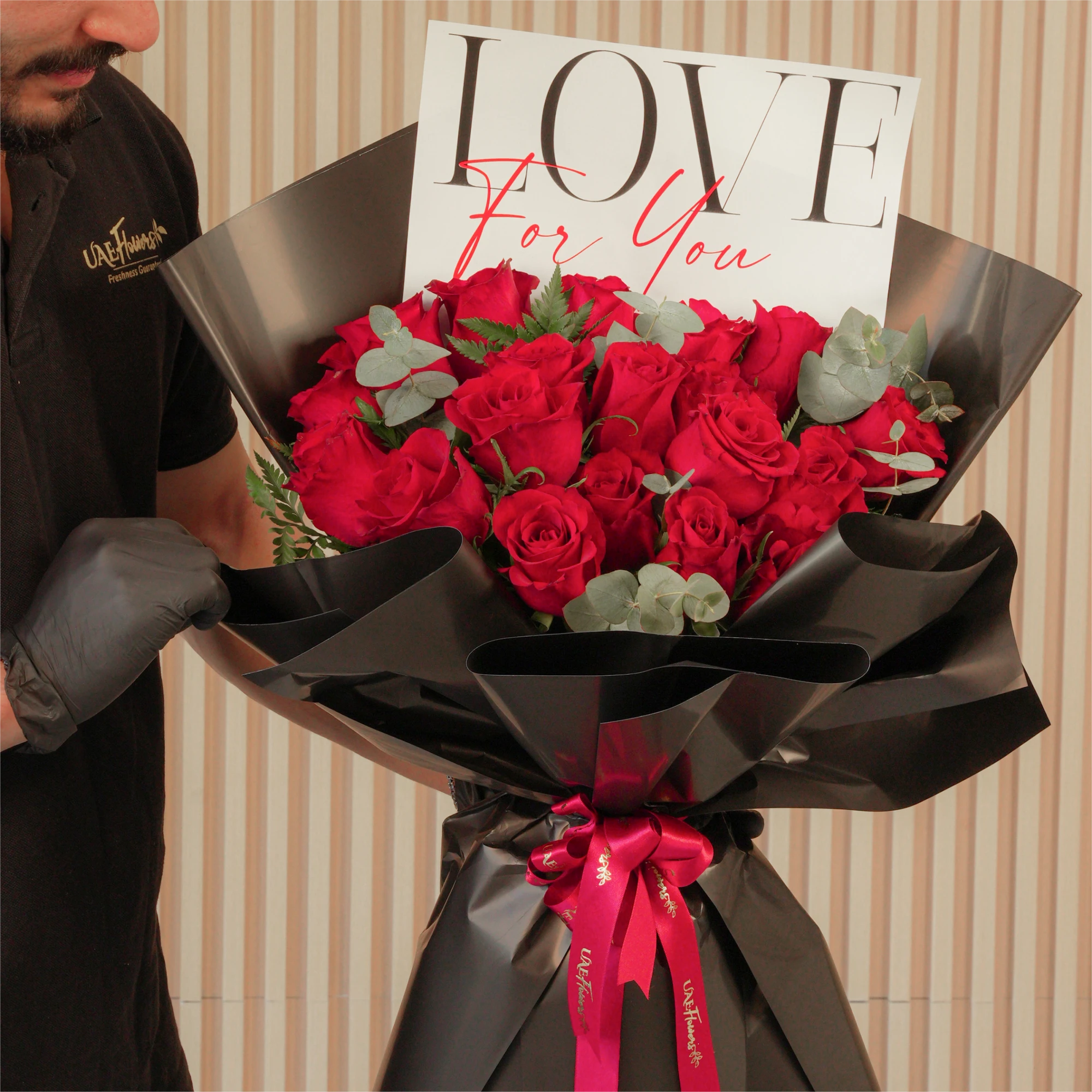 20 red roses with green fillers, wrapped in black and tied with red ribbons.
