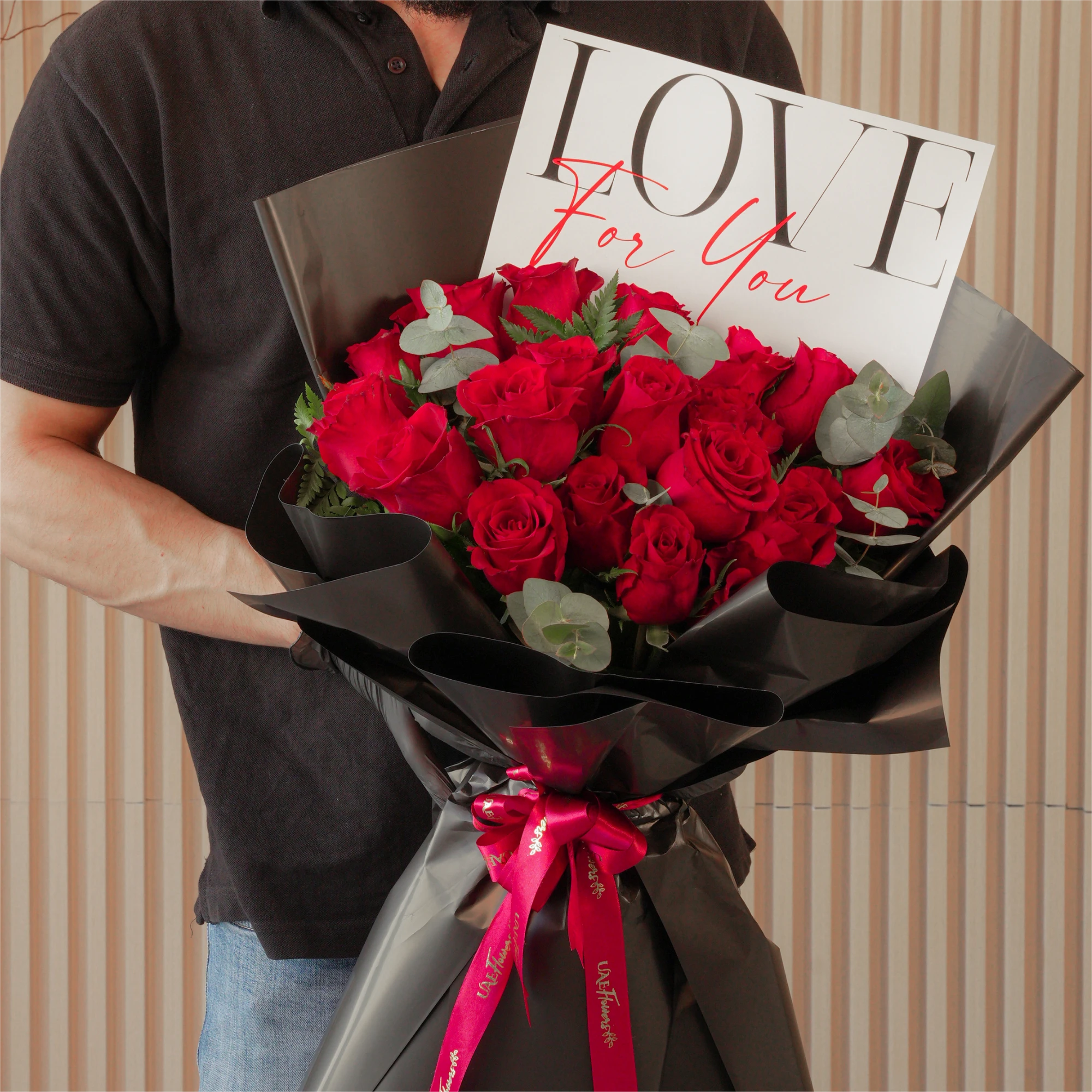 20 red roses with green fillers, wrapped in black and tied with red ribbons.
