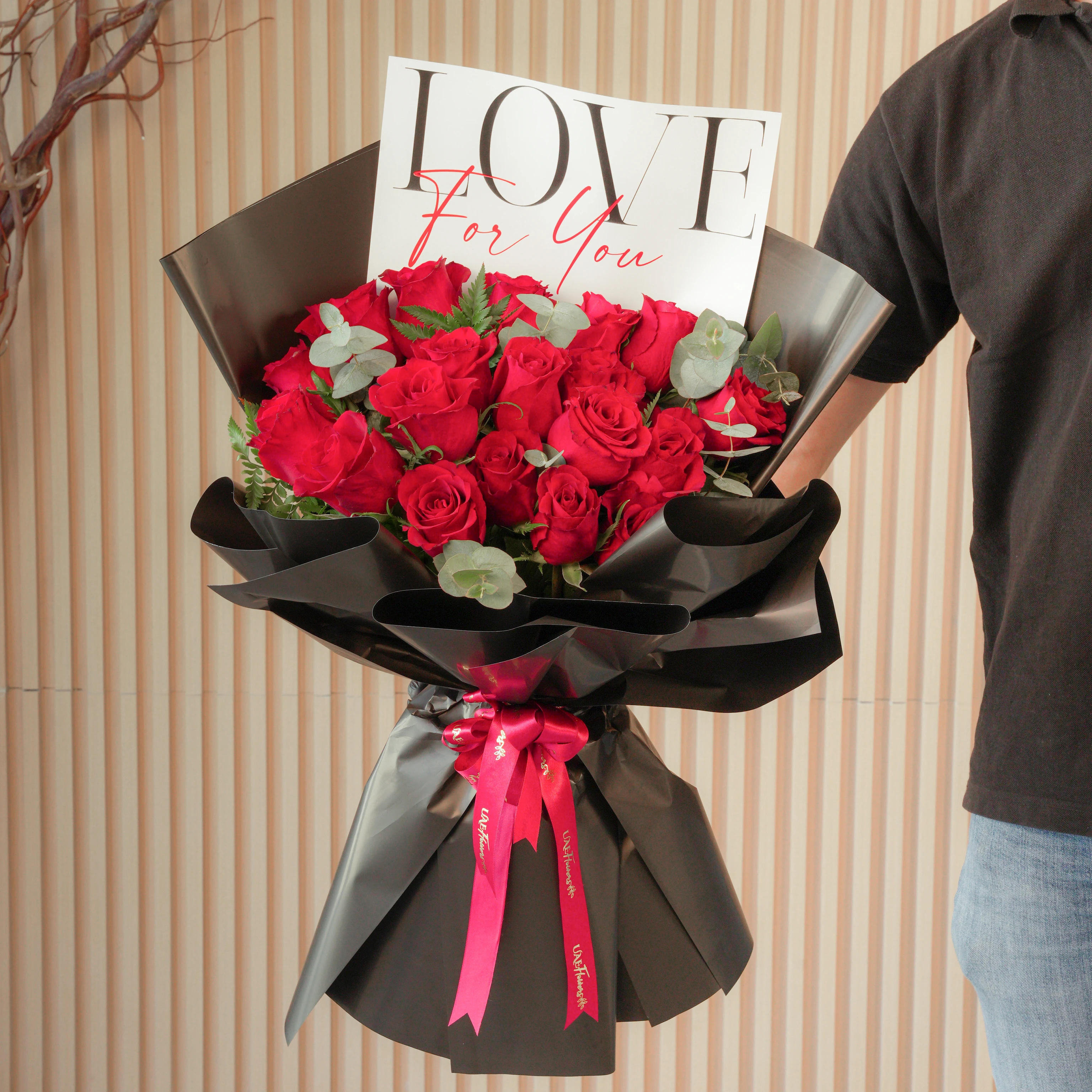 20 red roses with green fillers, wrapped in black and tied with red ribbons.