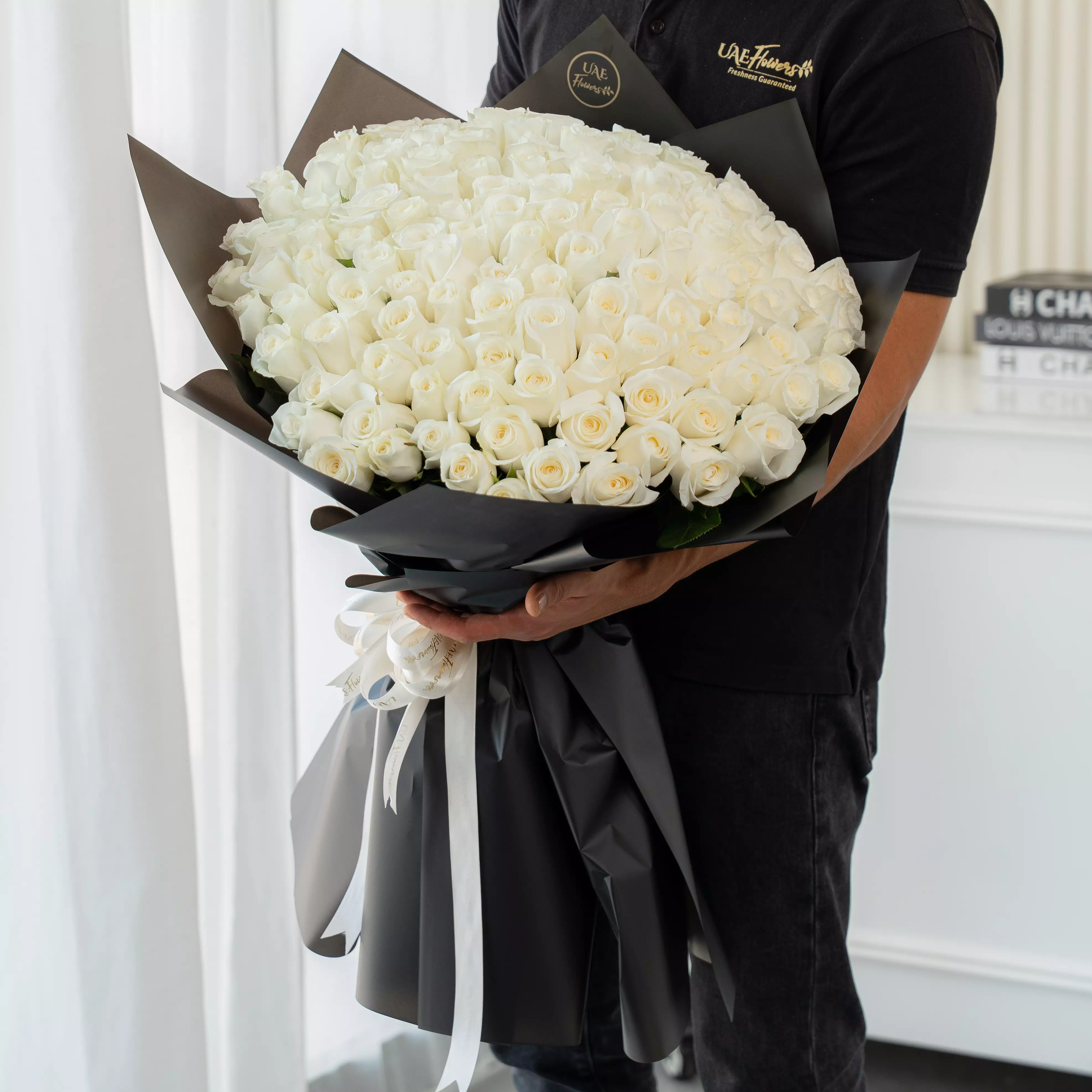 Bouquet of 100 white roses in black paper packing tied with ribbons