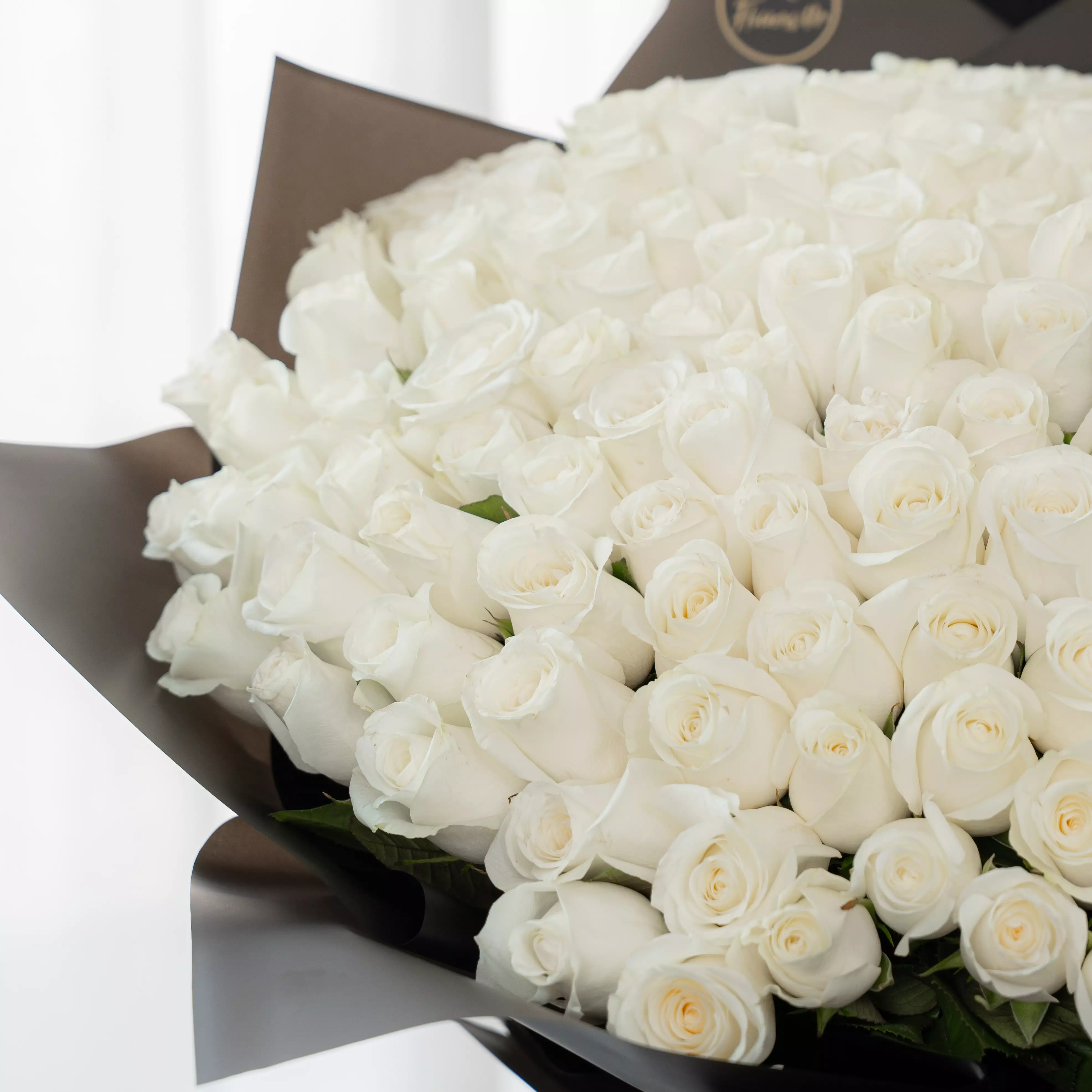 Bouquet of 100 white roses in black paper packing tied with ribbons