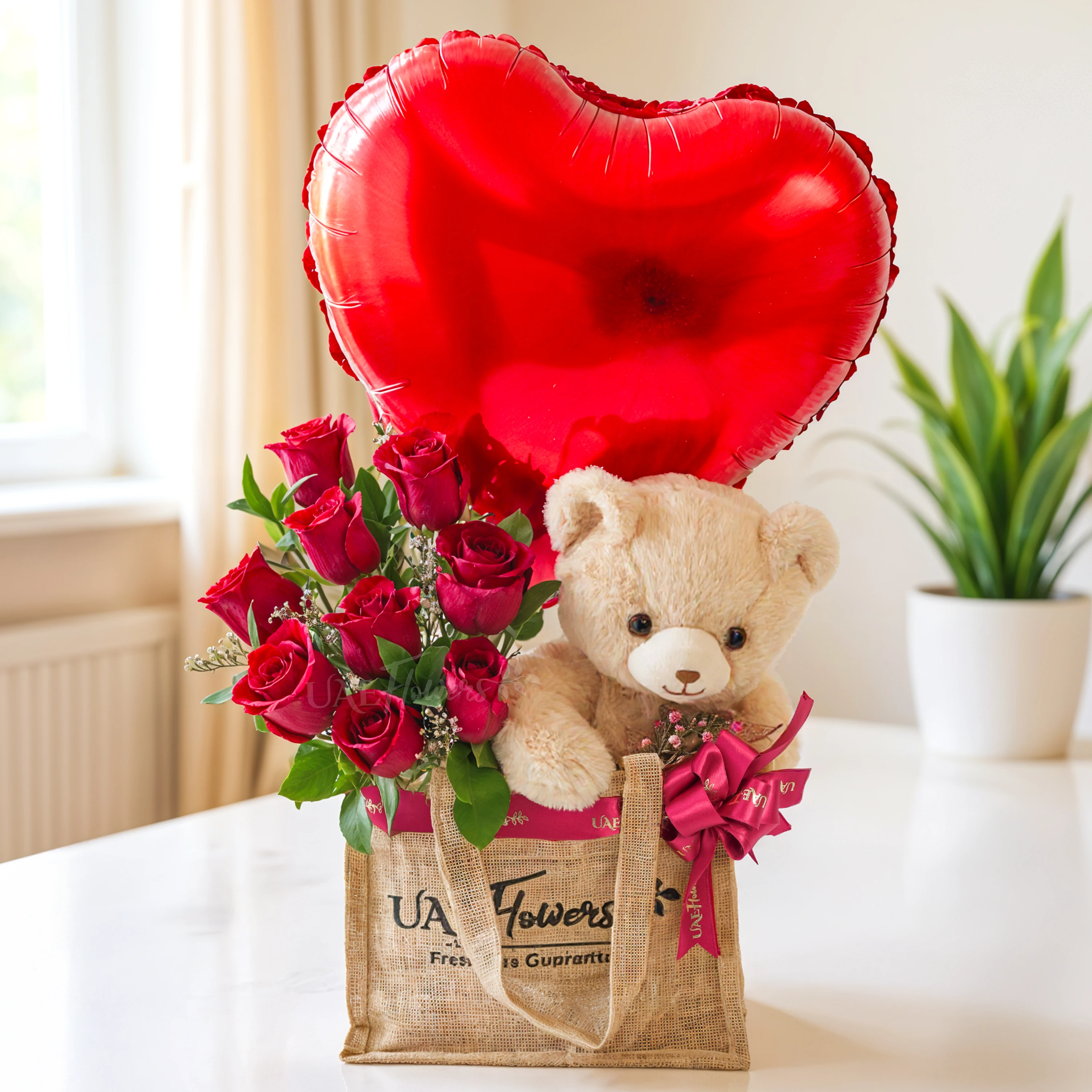 An arrangement of 7 red roses, small size teddy bear and hear shaped balloons in a jute bag