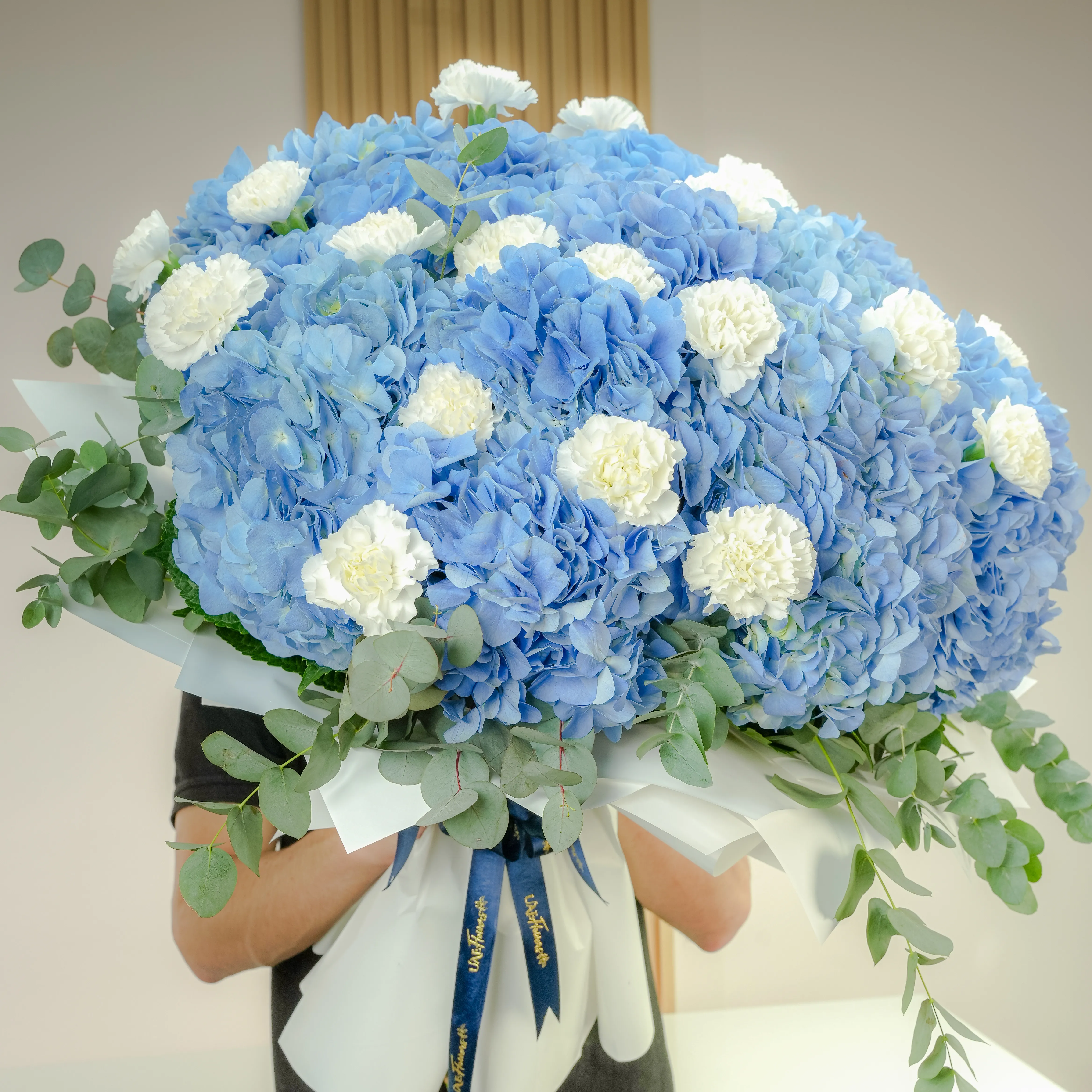 15 blue hydrangeas, 20 white carnations, and fillers, wrapped in paper with ribbon