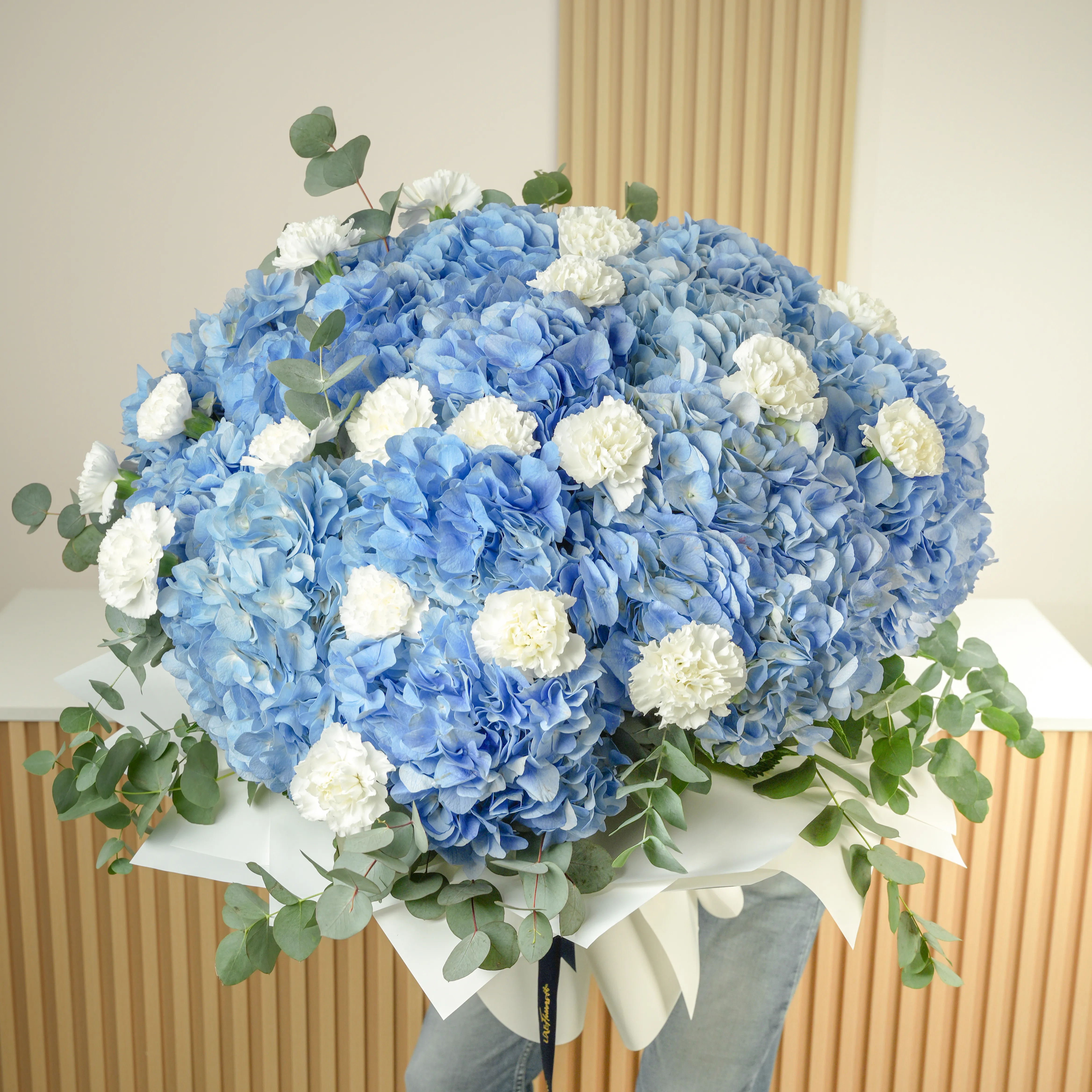 15 blue hydrangeas, 20 white carnations, and fillers, wrapped in paper with ribbon