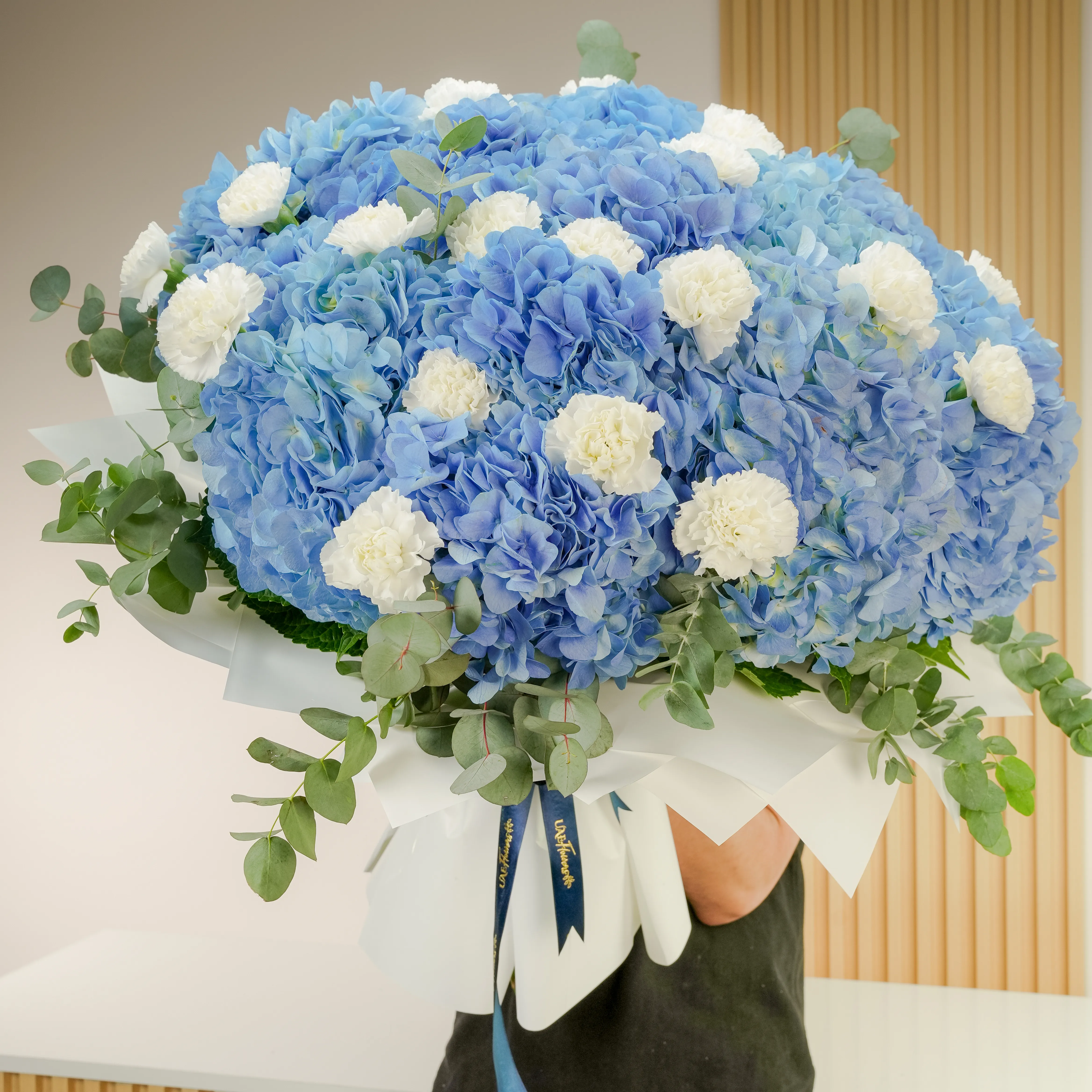 15 blue hydrangeas, 20 white carnations, and fillers, wrapped in paper with ribbon