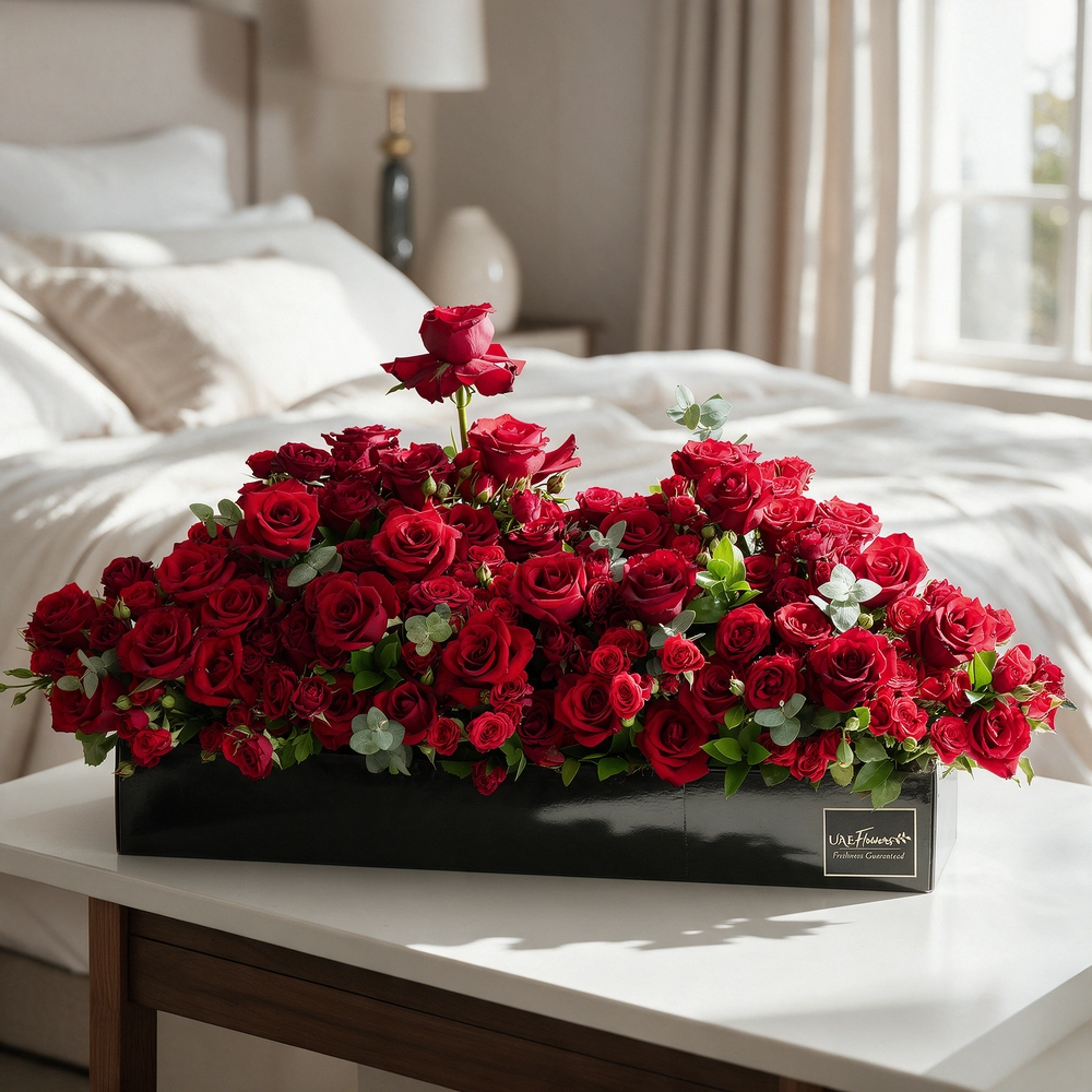 Arrangement of 50 red roses and 30 red spray roses with green fillers in a long black box.