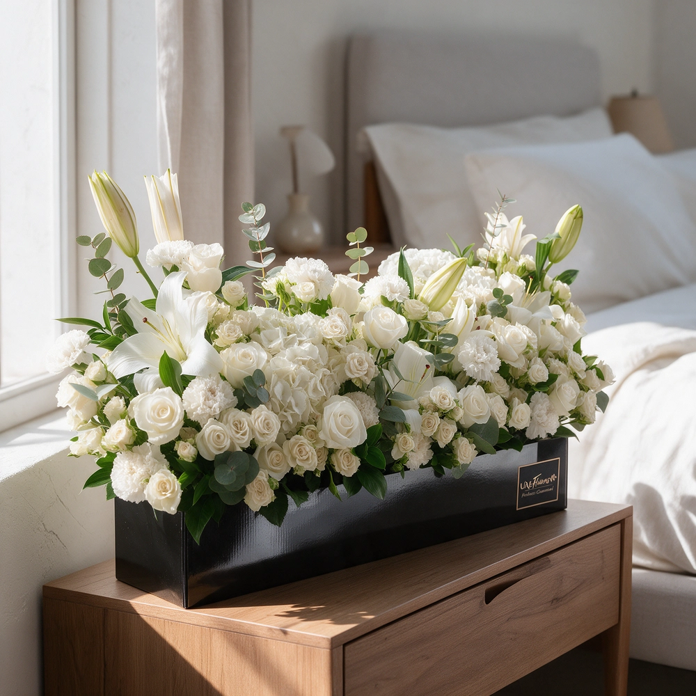 Arrangement of 5 white lilies, 20 white roses, 20 white spray roses, 10 white carnations and 2 white hydrangeas with green fillers in a long black box.