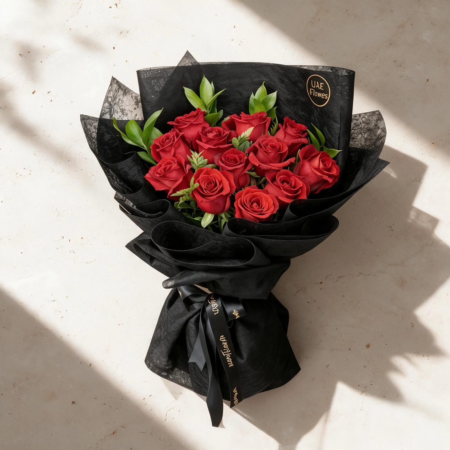 Bouquet of 12 red roses with green fillers in black wrapping paper.