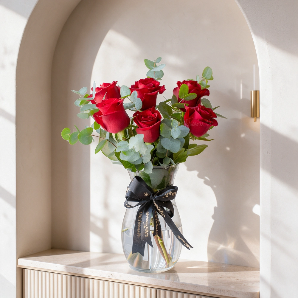 6 red roses arranged in a glass vase with eucalyptus