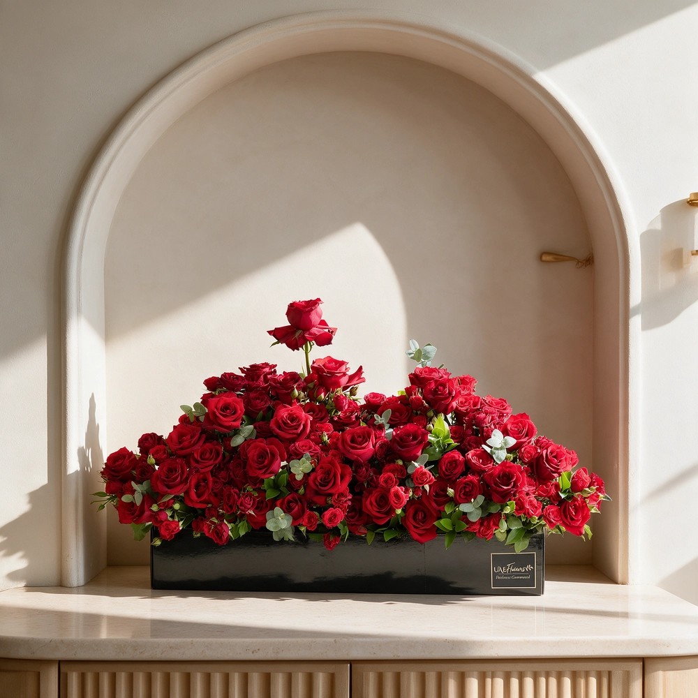 Arrangement of 50 red roses and 30 red spray roses with green fillers in a long black box.